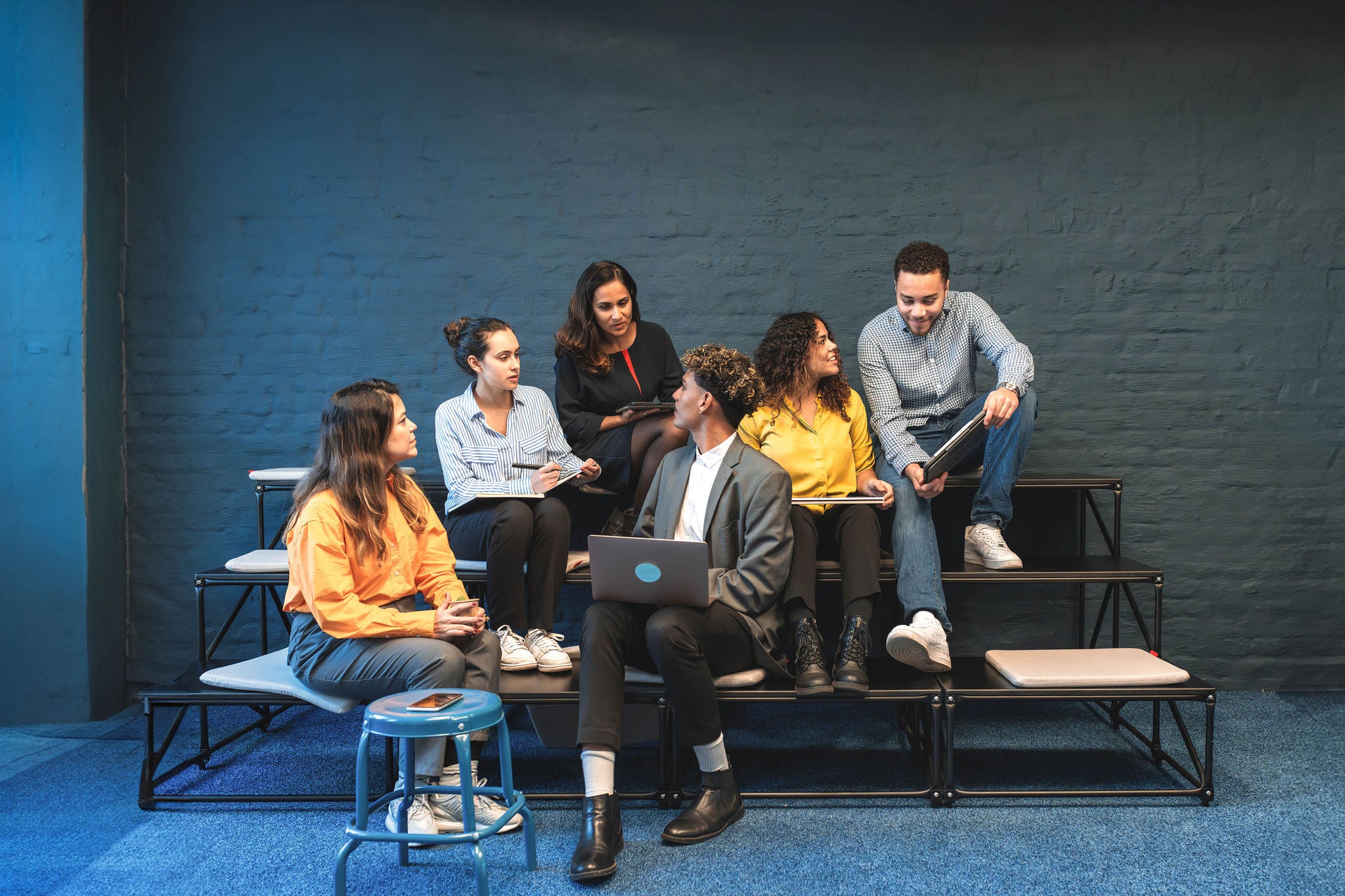 group of young business people sitting with laptops and digital tablets on steps in meeting room and talking