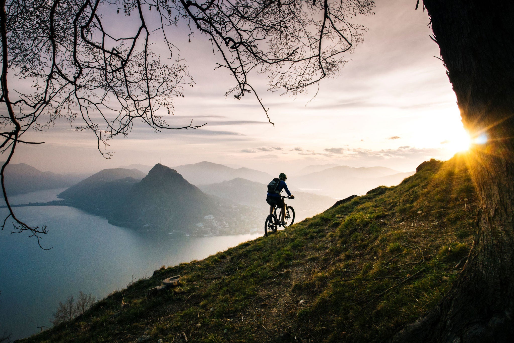 Mountain biker traverses steep mountain slope above lake