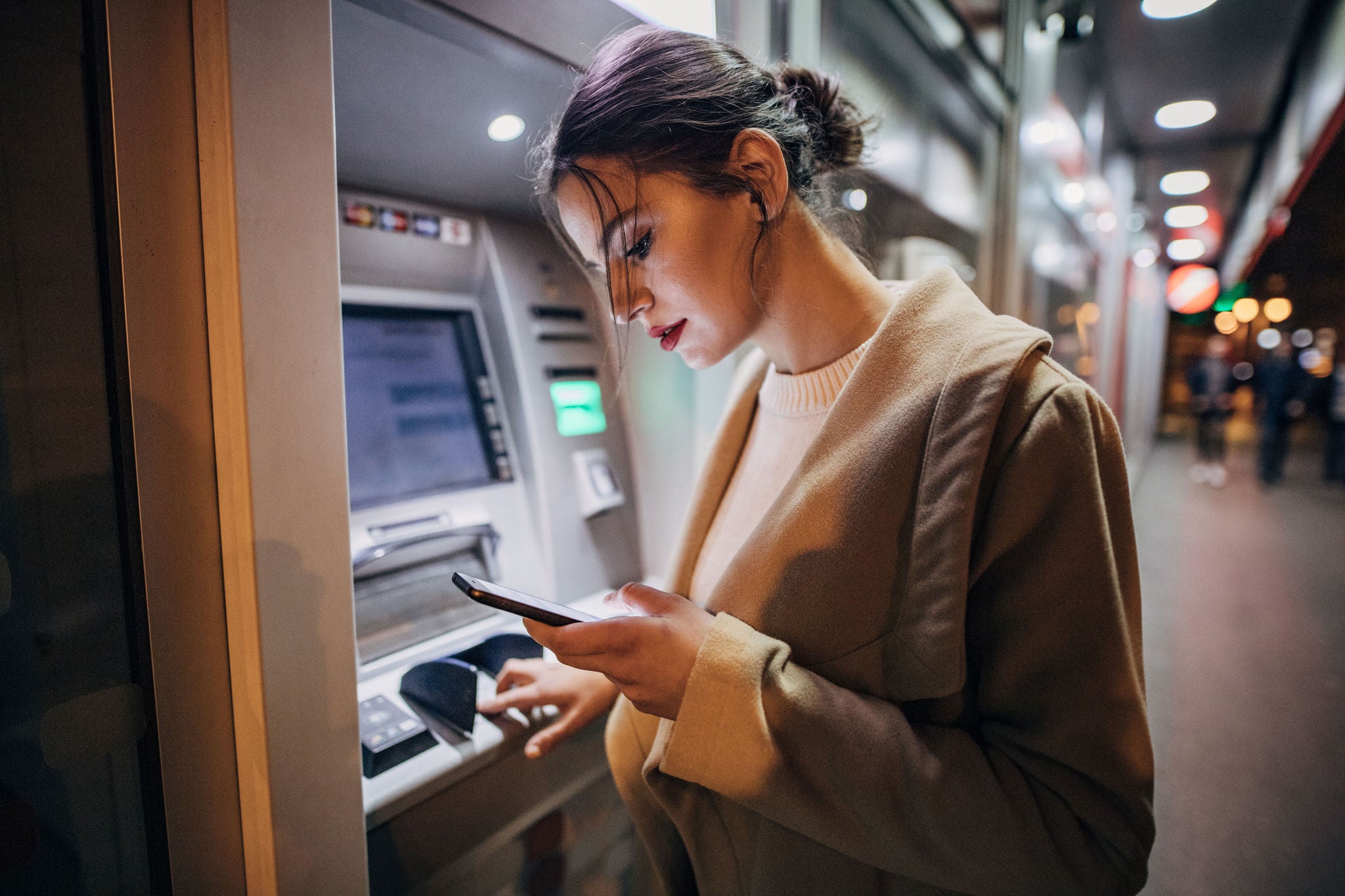 One young beautiful young teenage girl using ATM machine and smart phone in the city