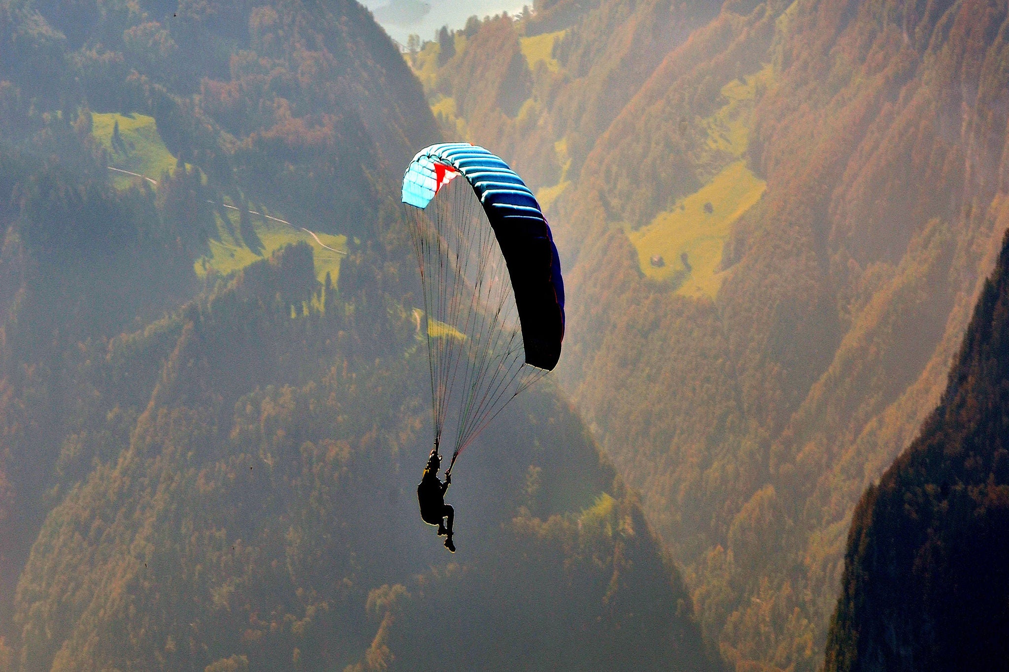 A man is paragliding between mountains