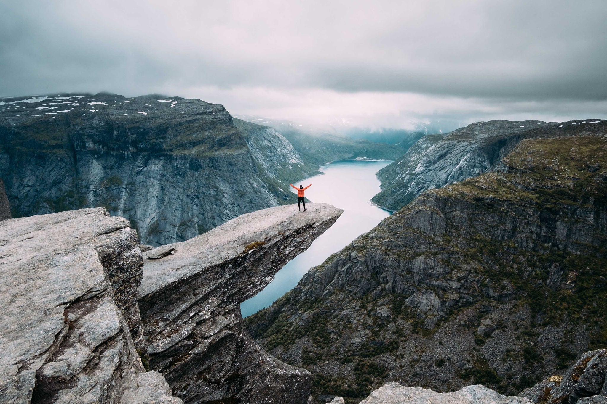 Person på Trolltunga i Vestlandet, strekker ut armene omgitt av storslått natur.