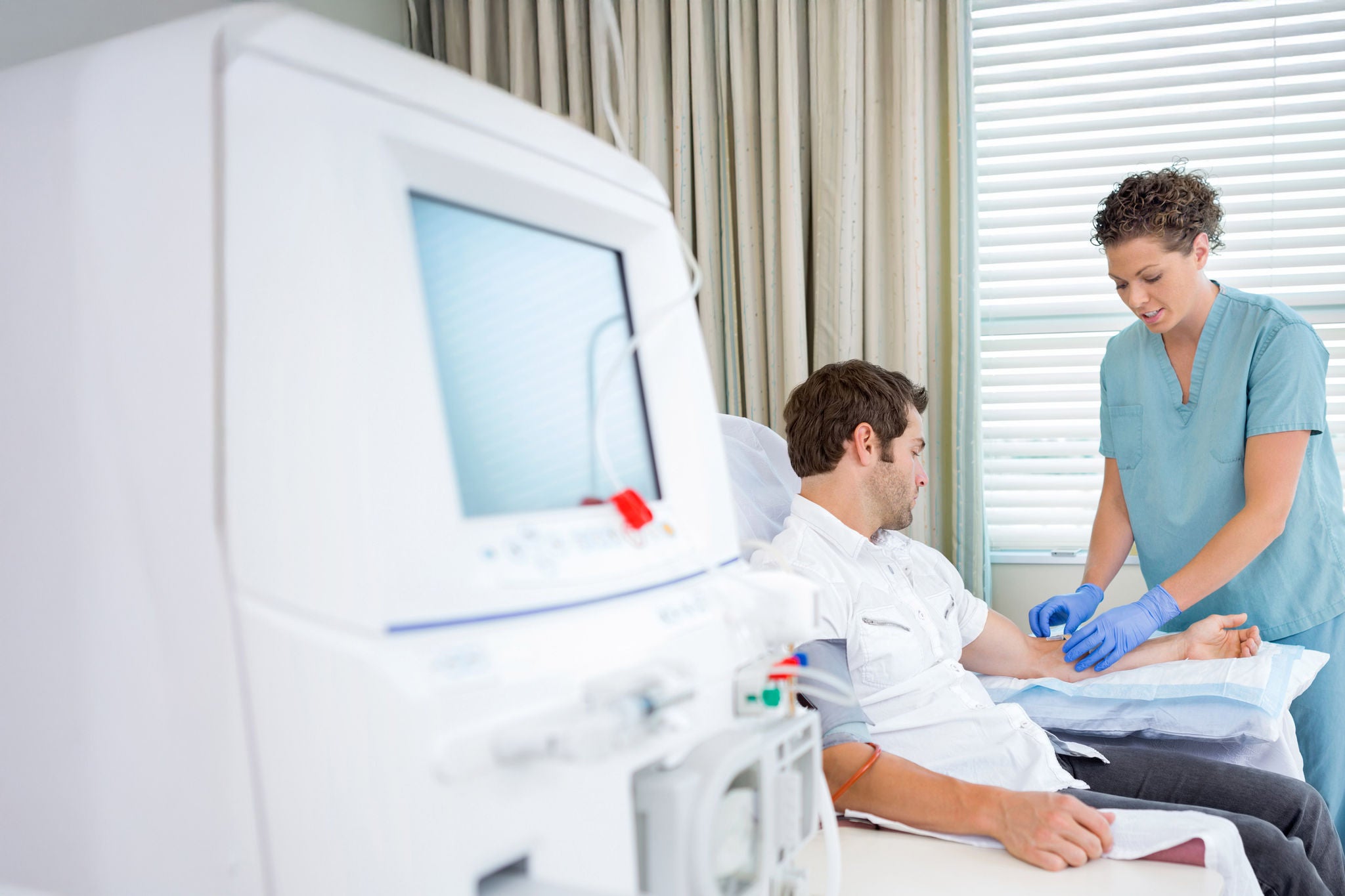 Mid adult female nurse injecting patient for renal dialysis treatment in hospital room