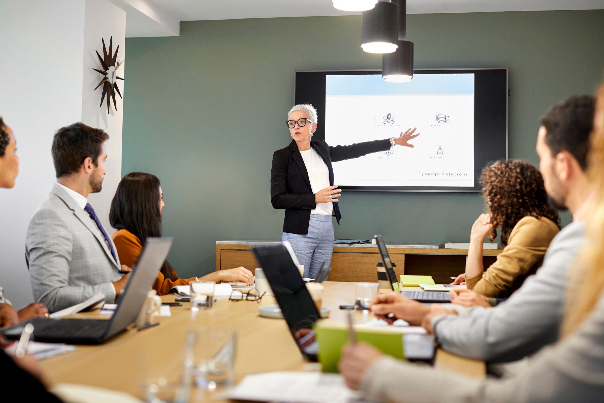 Senior businesswoman giving presentation to team. Male and female professionals are planning strategy in meeting. They are in board room at office.