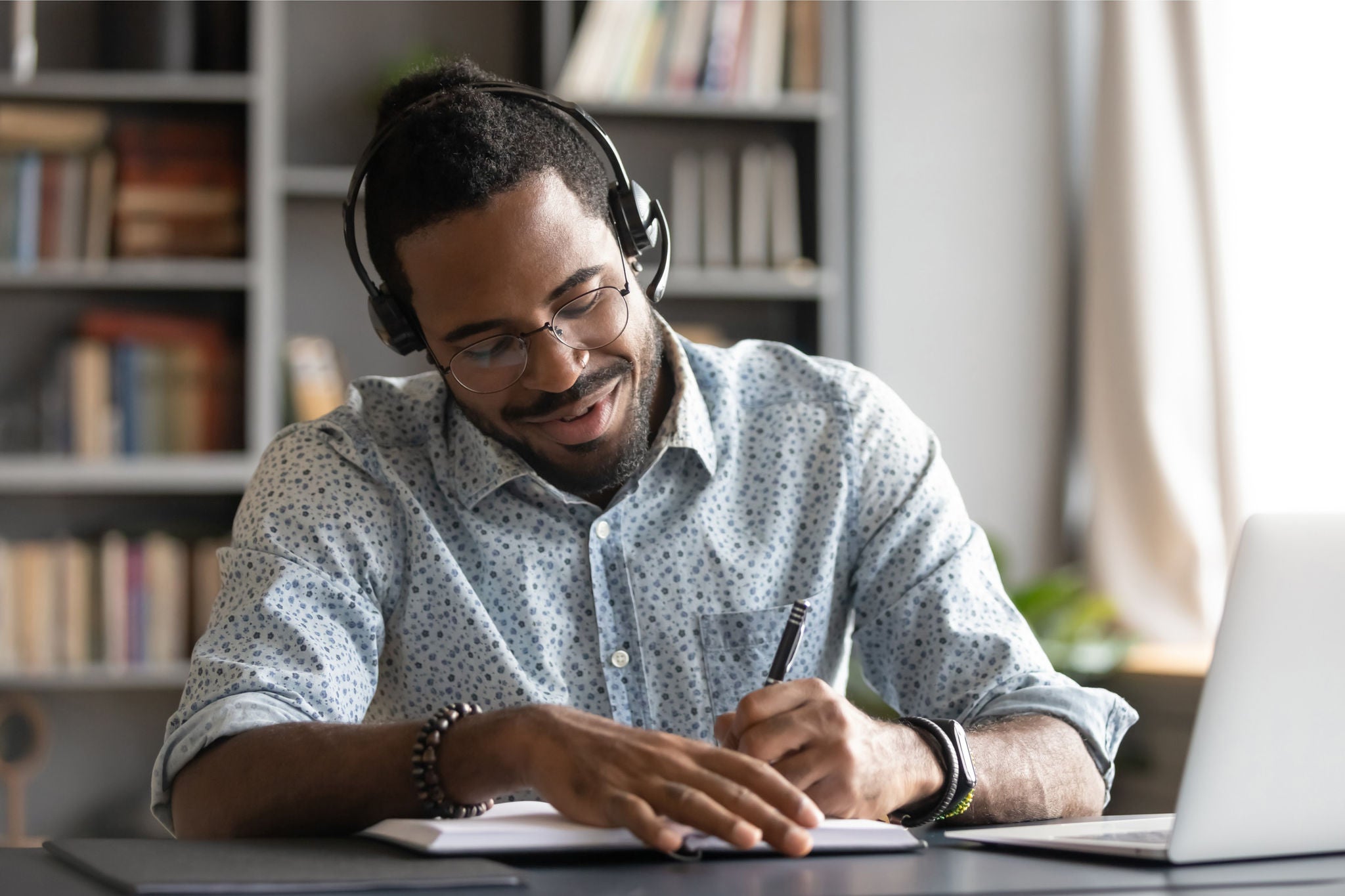 Man wearing head phone taking notes while using laptop