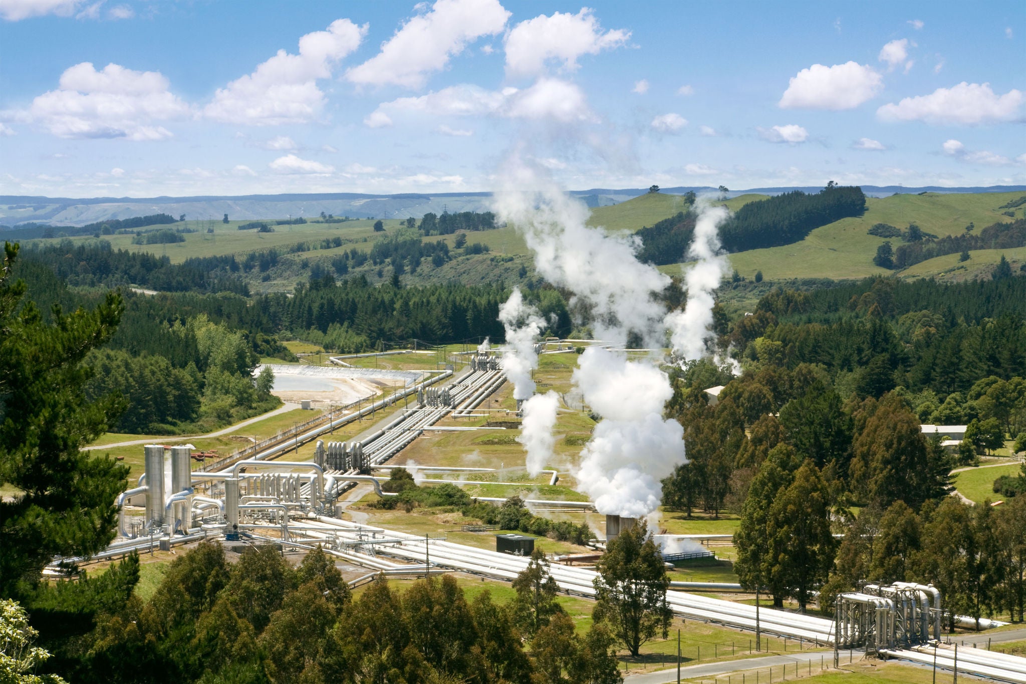 A geothermal power plant situated in a lush, green landscape with rolling hills and forests in the background.