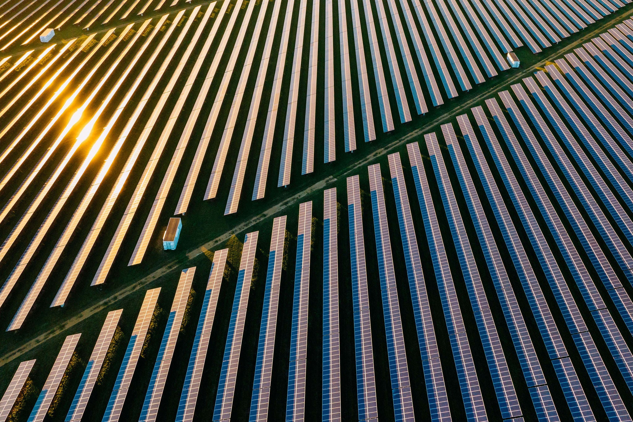 Aerial view of a large solar farm with numerous rows of solar panels aligned in parallel.