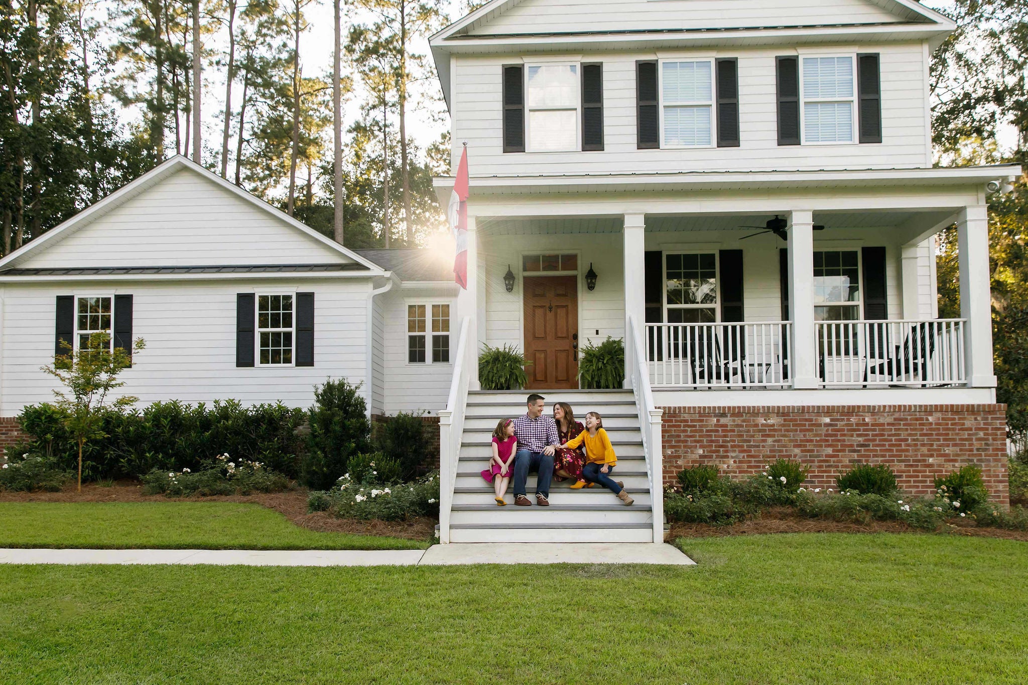 Family of Four With Daughters Sitting on the Steps Outside their Home Laughing Together