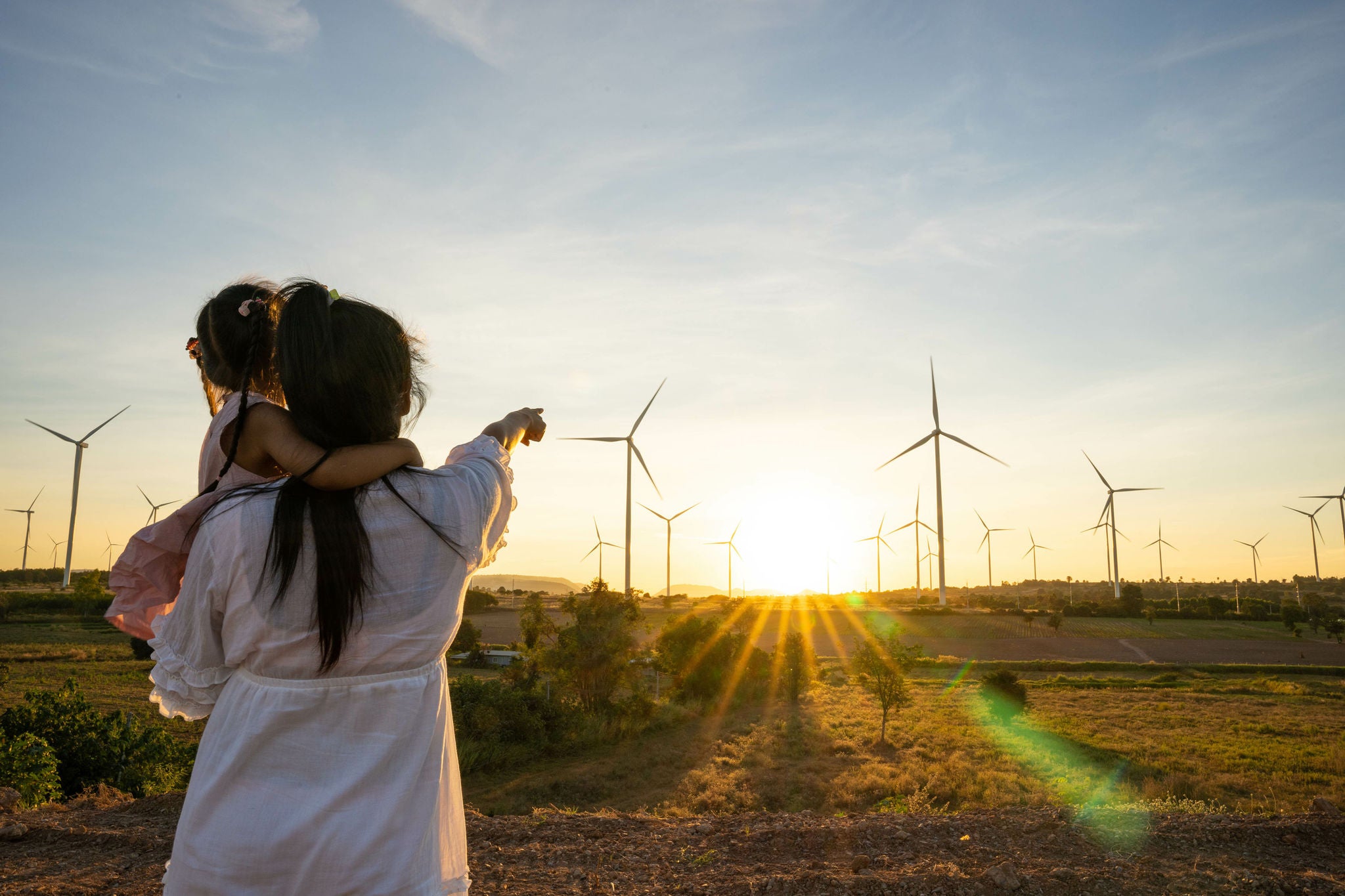 Mother points at wind turbines while holding daughter