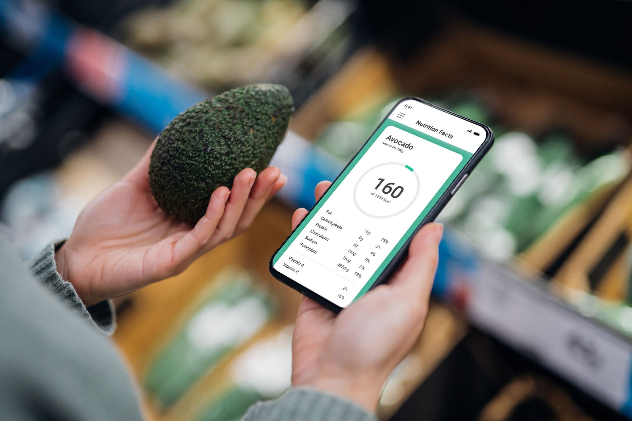 Woman shopping for fresh fruit and vegetables in supermarket. Holding mobile phone and avocado. Healthy eating lifestyle concept. Using mobile app to track nutrition and count calories.