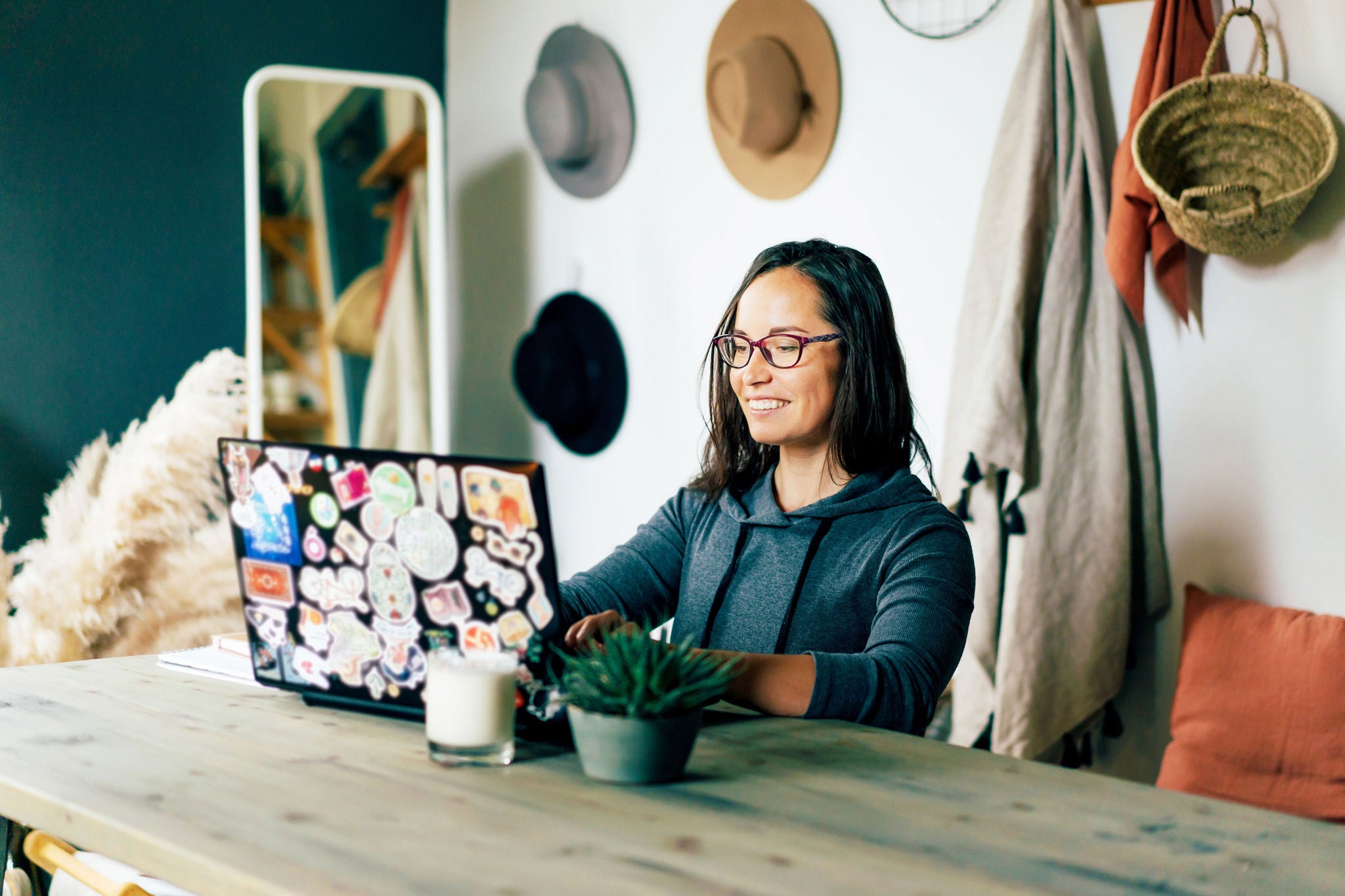 Happy brunette woman works on a laptop decorated with pictures in the interior of a cozy living room of her apartment. Remote work from home. Online trainings and professional development.