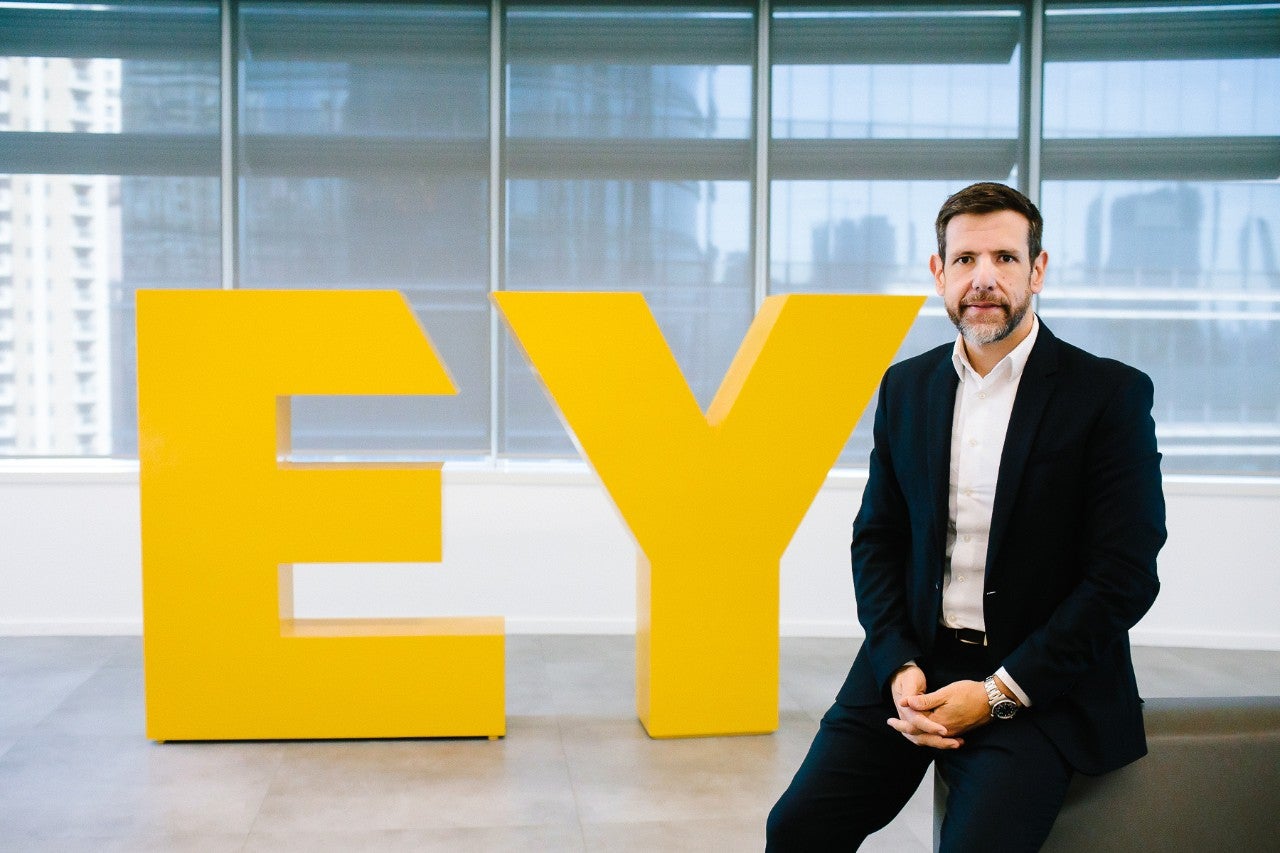 Ricardo Assumpção em fotografia ao lado do Logo da EY