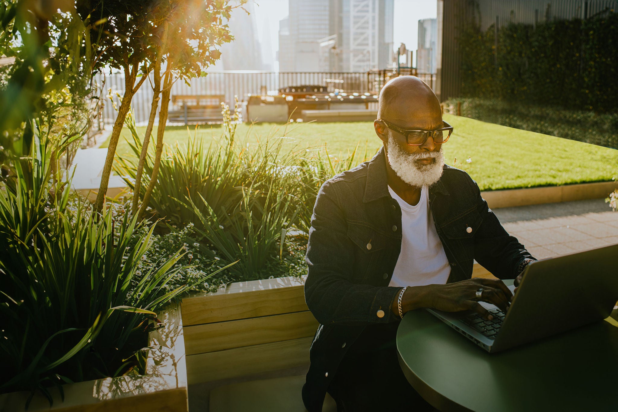 A man sits outside on a rooftop terrace and uses a laptop 