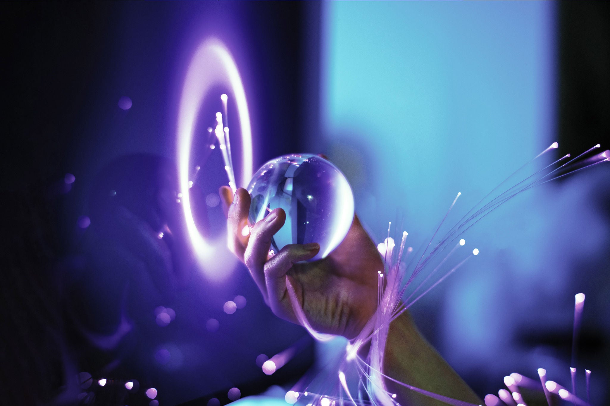 A hand wrapped in glowing optical fibers, holding a crystal ball, symbolizing technology and foresight
