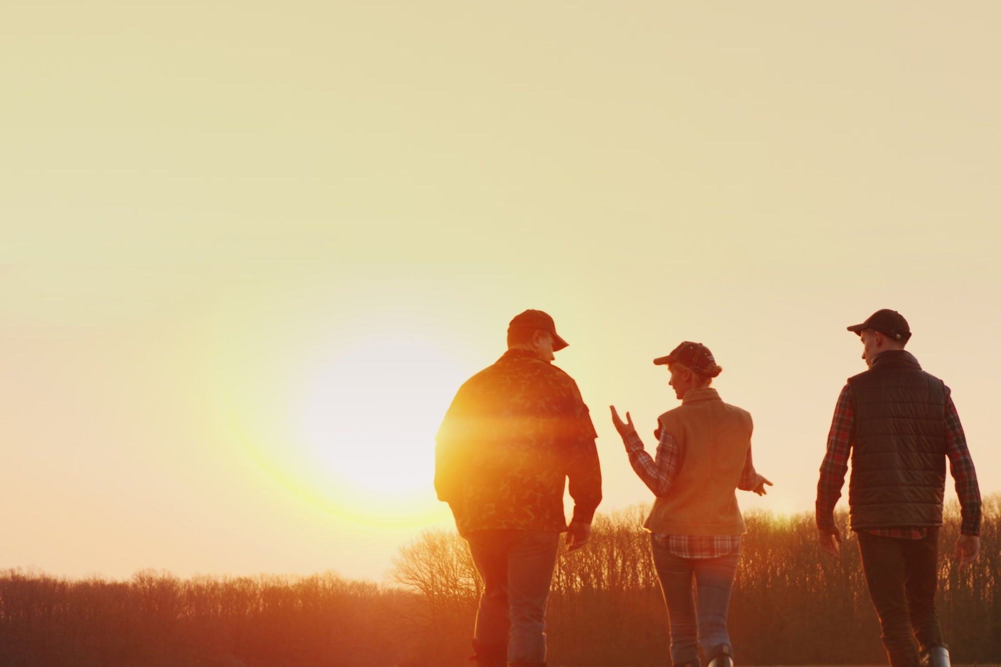 Three farmers go ahead on a plowed field at sunset. Young team of farmers.