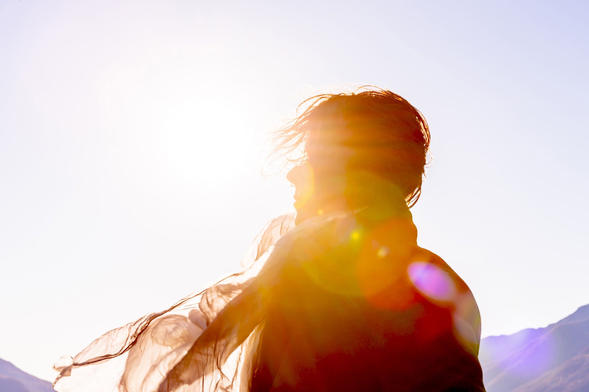Woman with moving hair and scarf in sunlight in a windy day