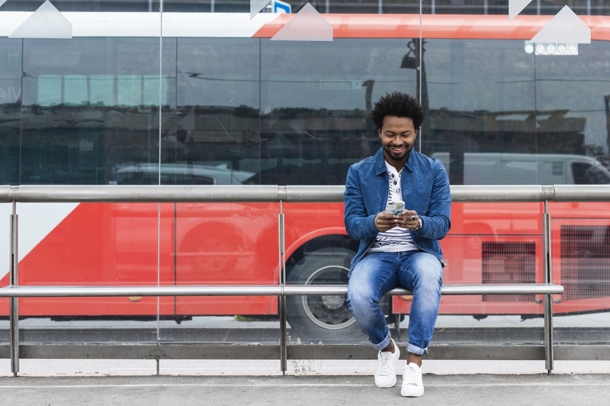 EY – Homme adulte d’âge moyen distingué et souriant qui utilise son cellulaire alors qu’il est assis à un arrêt d’autobus