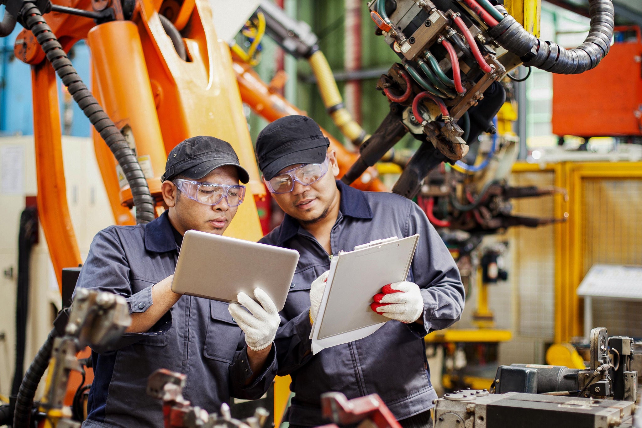 Two engineers checking production on a tablet and notepad