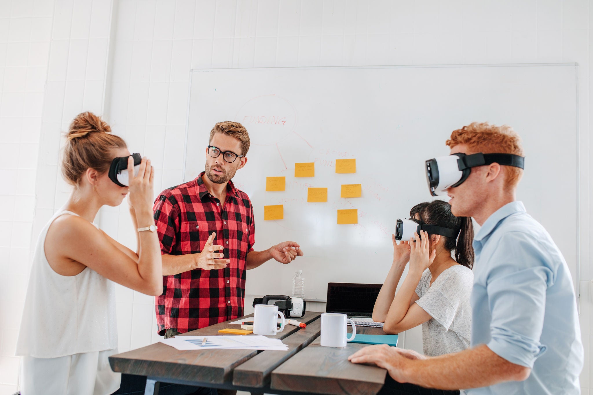 Young men and women sitting at a table with virtual reality goggles. Business team testing virtual reality headset in office meeting.