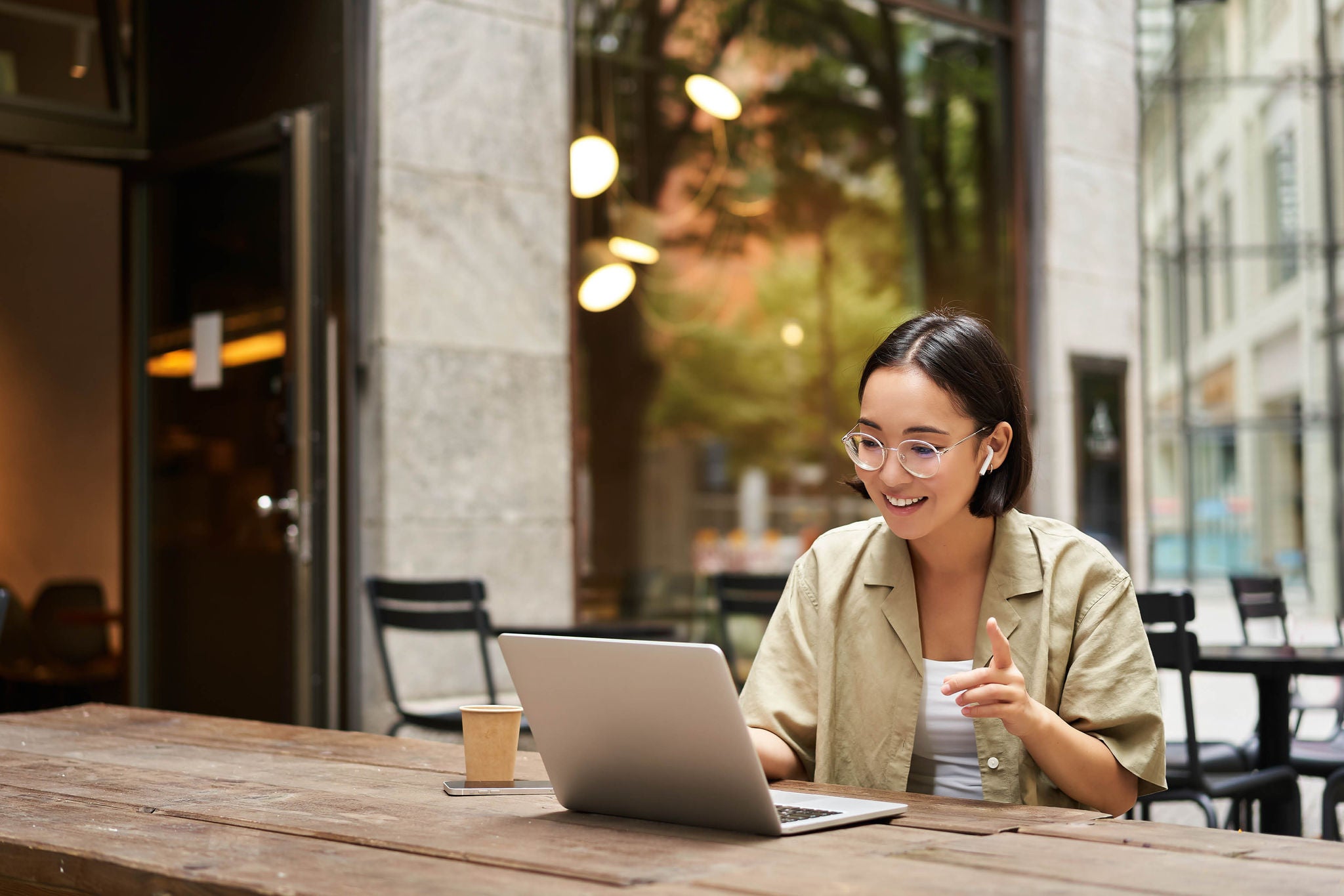 EY - Young woman sitting on online meeting in outdoor cafe