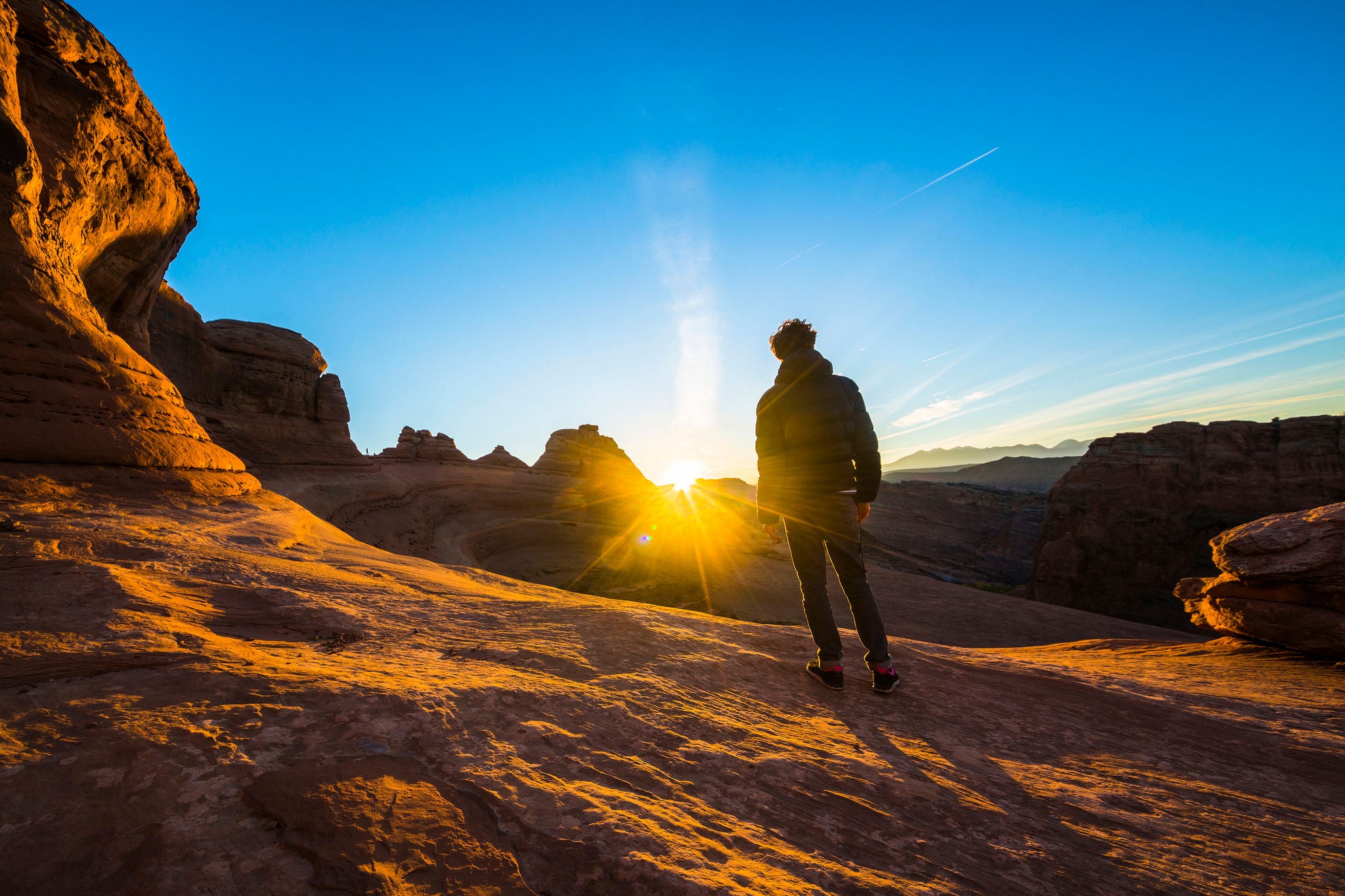 traveler and hiker, admiring the sunrise in the red canyon near by Delicate Arch at sunrise. The Arches National Monument, Utah, USA, North America. Unique geological formation.