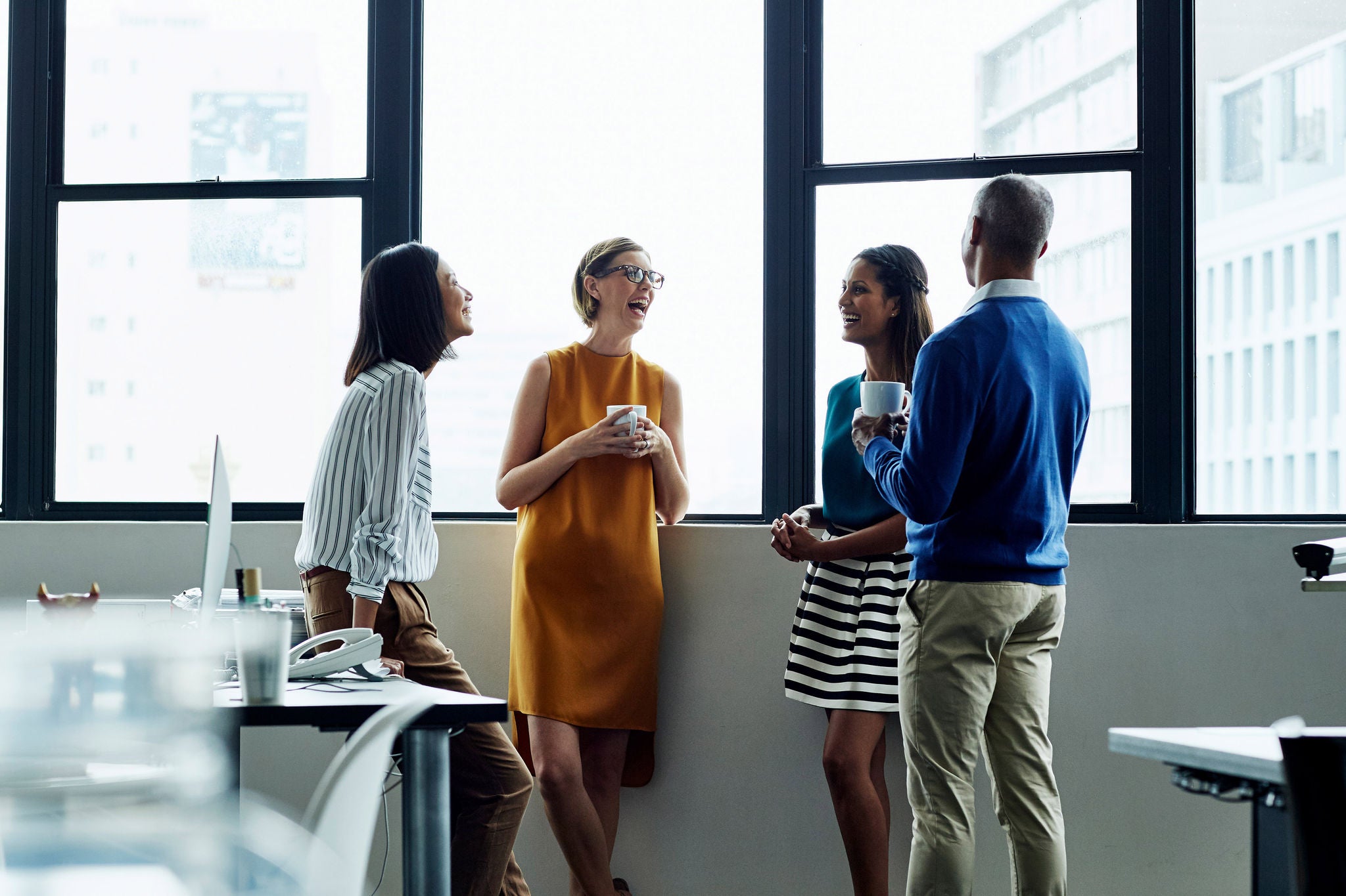 A group of coworkers talking and laughing by the office window.