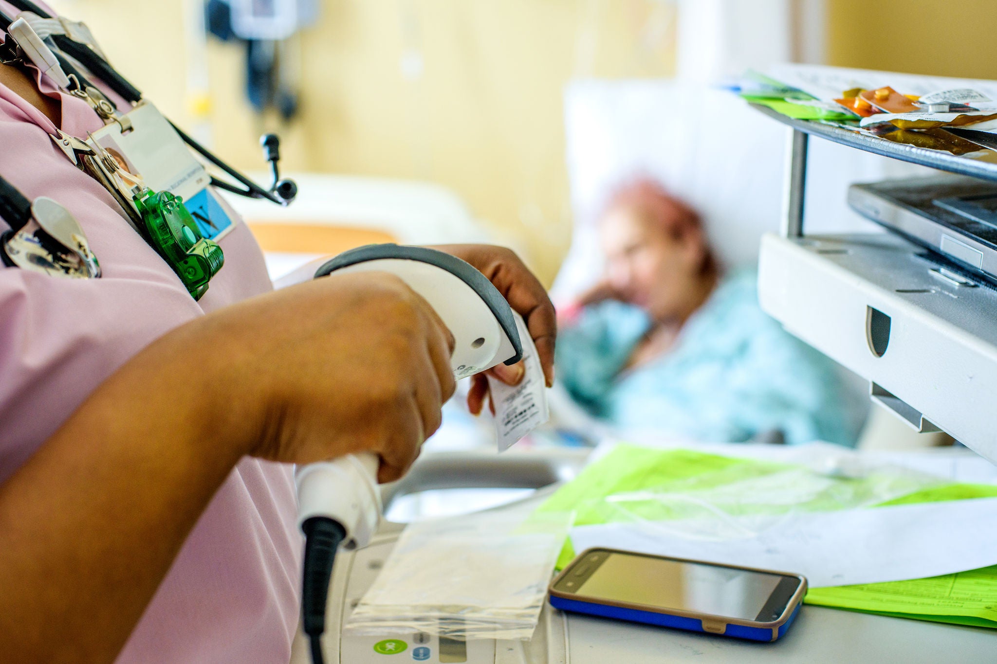 Nurse working in hospital, patient on bed in background