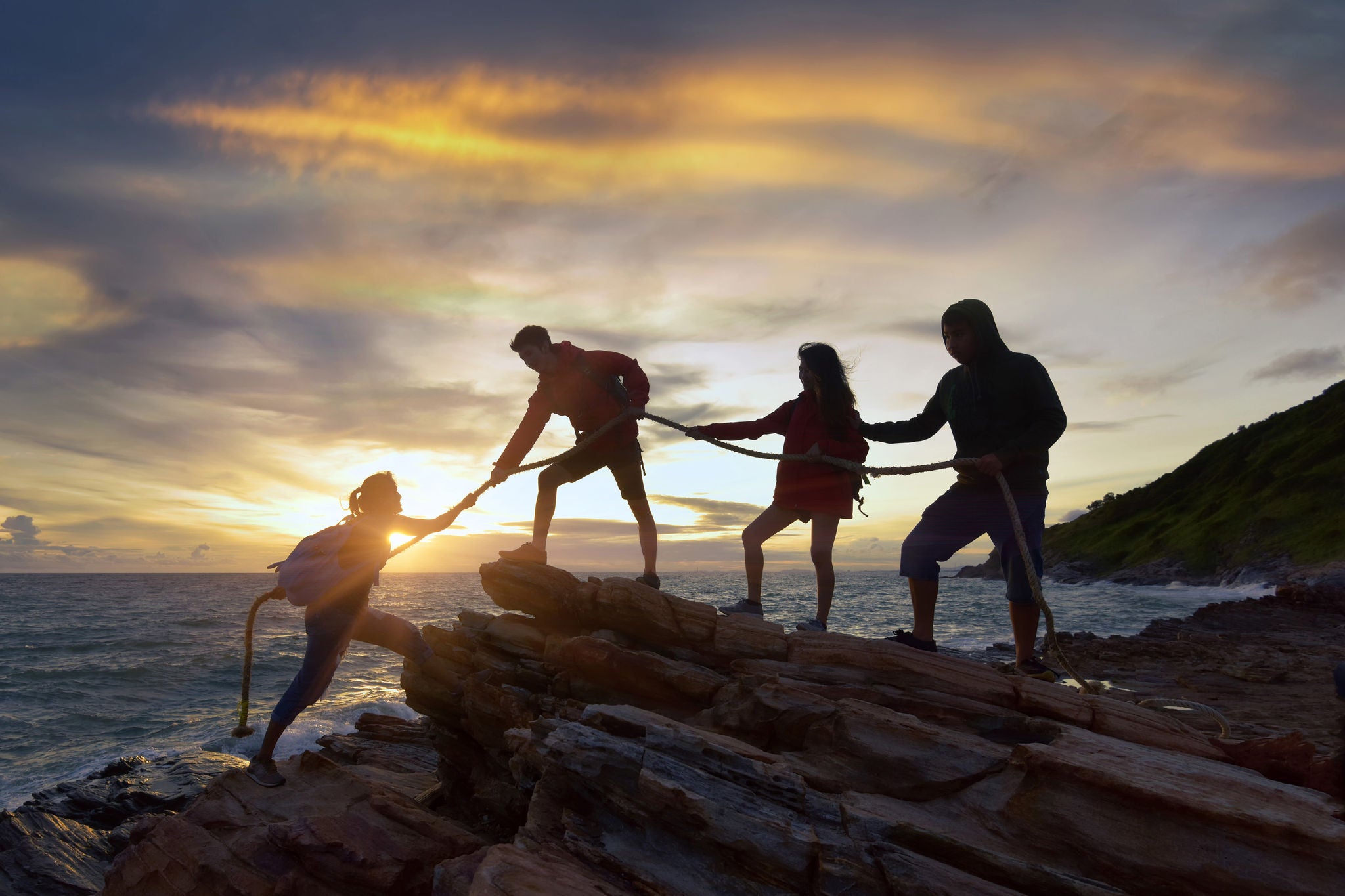 hikers helping a colleague climb up a cliff with rope