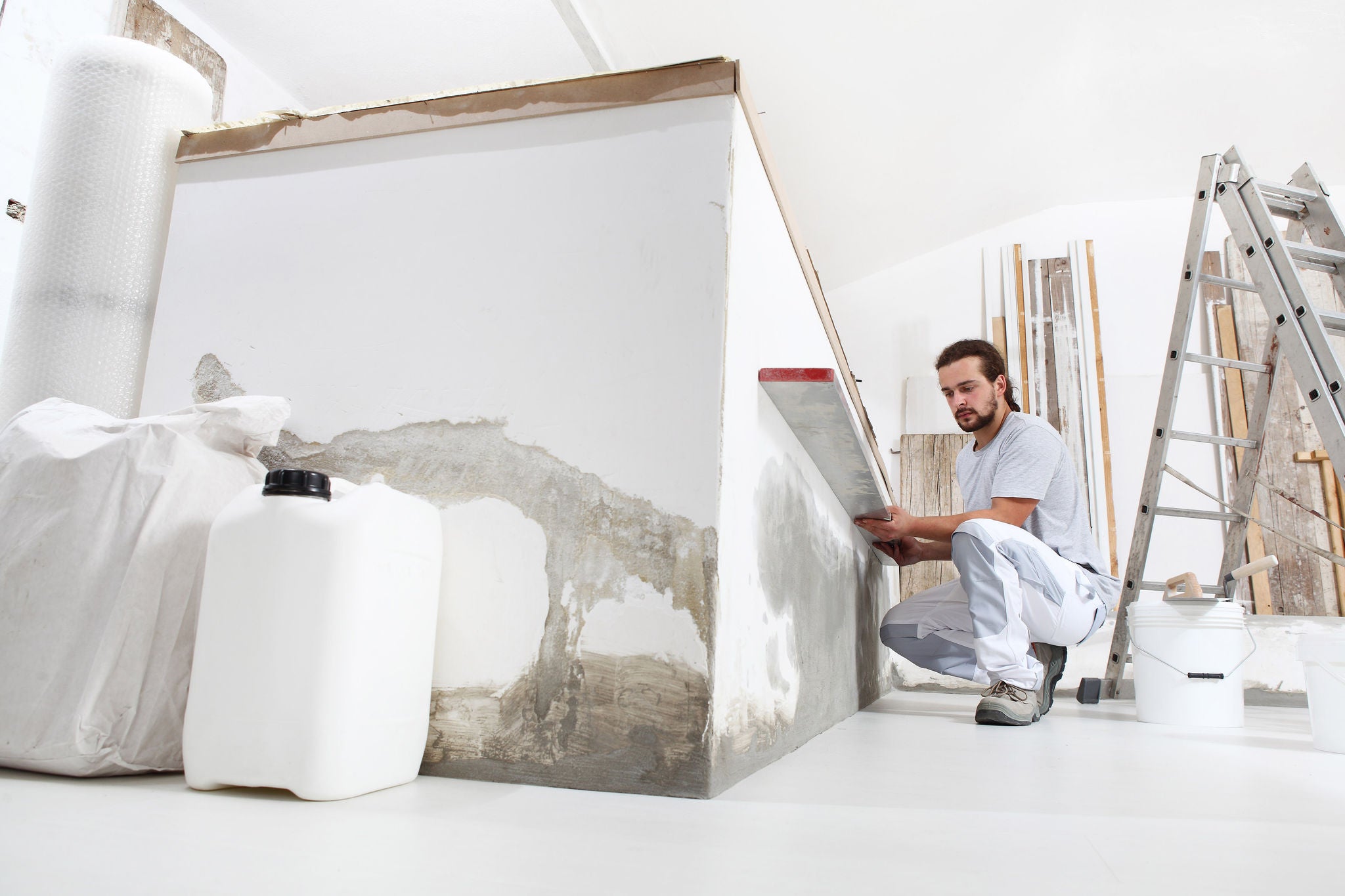 Bauarbeiter Stuckateur Mann schaut auf die Wasserwaage und prÃ¼ft die Wand auf der Baustelle der Hausrenovierung mit Werkzeugen und Baumaterialien auf dem Boden