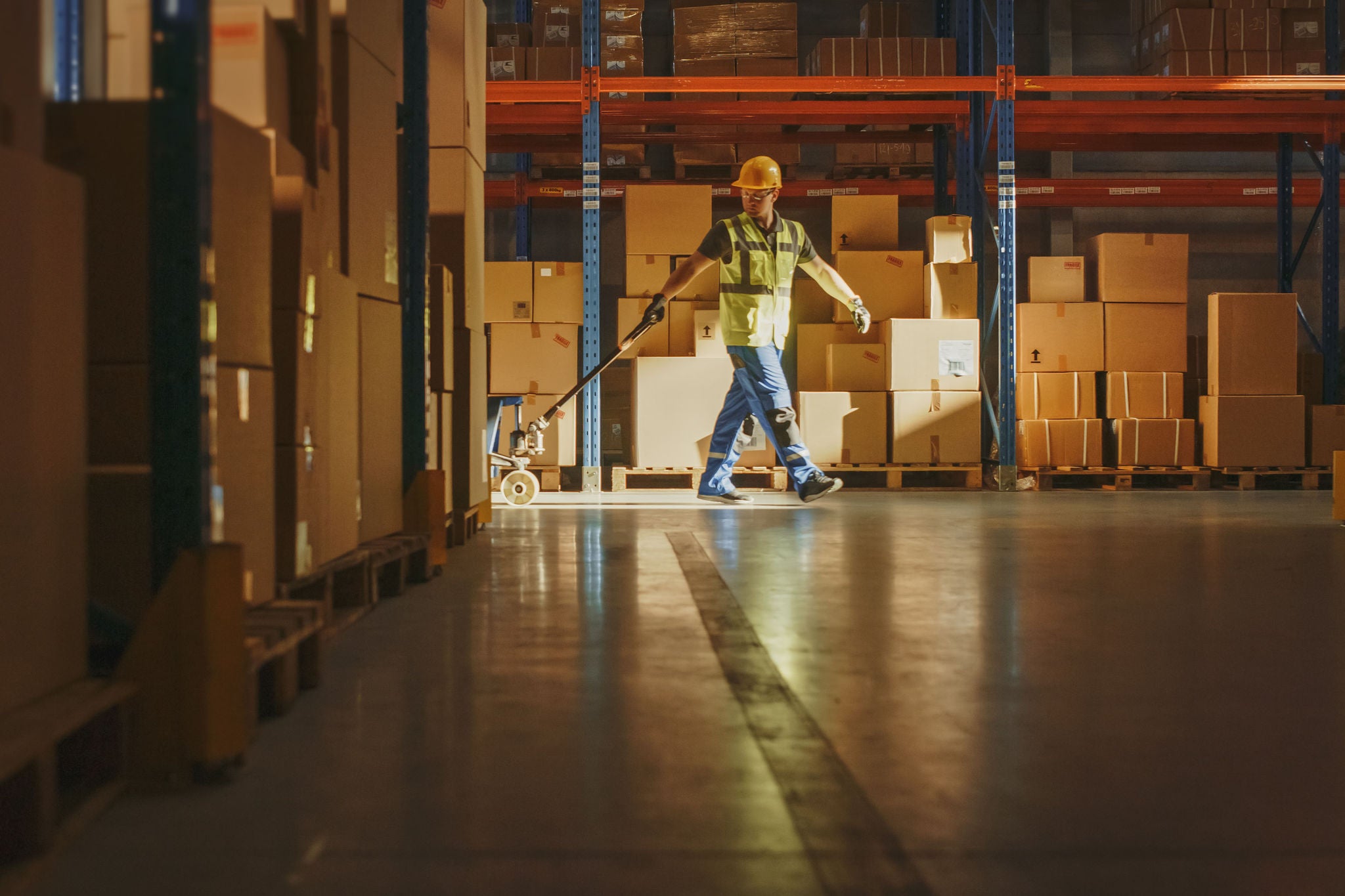 Worker moves cardboard boxes using hand pallet truck