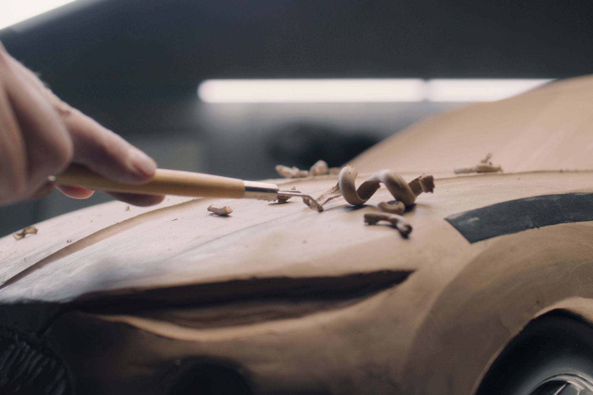 Close-up shot of male automotive designer working on futuristic car model from plasticine clay with rake. Future design of new generation electric car. Work in modern car design studio.