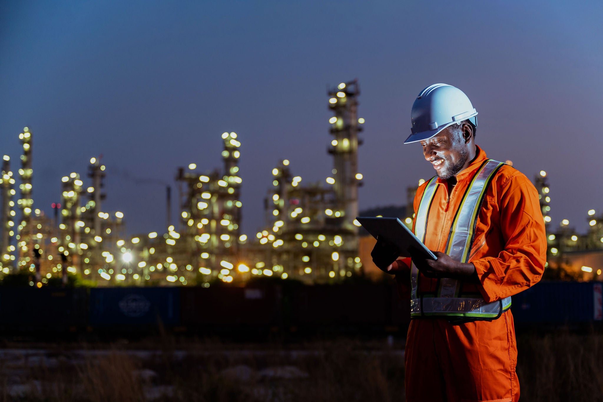 African construction engineer working on tablet inspecting the build project in oil refinery plant at night