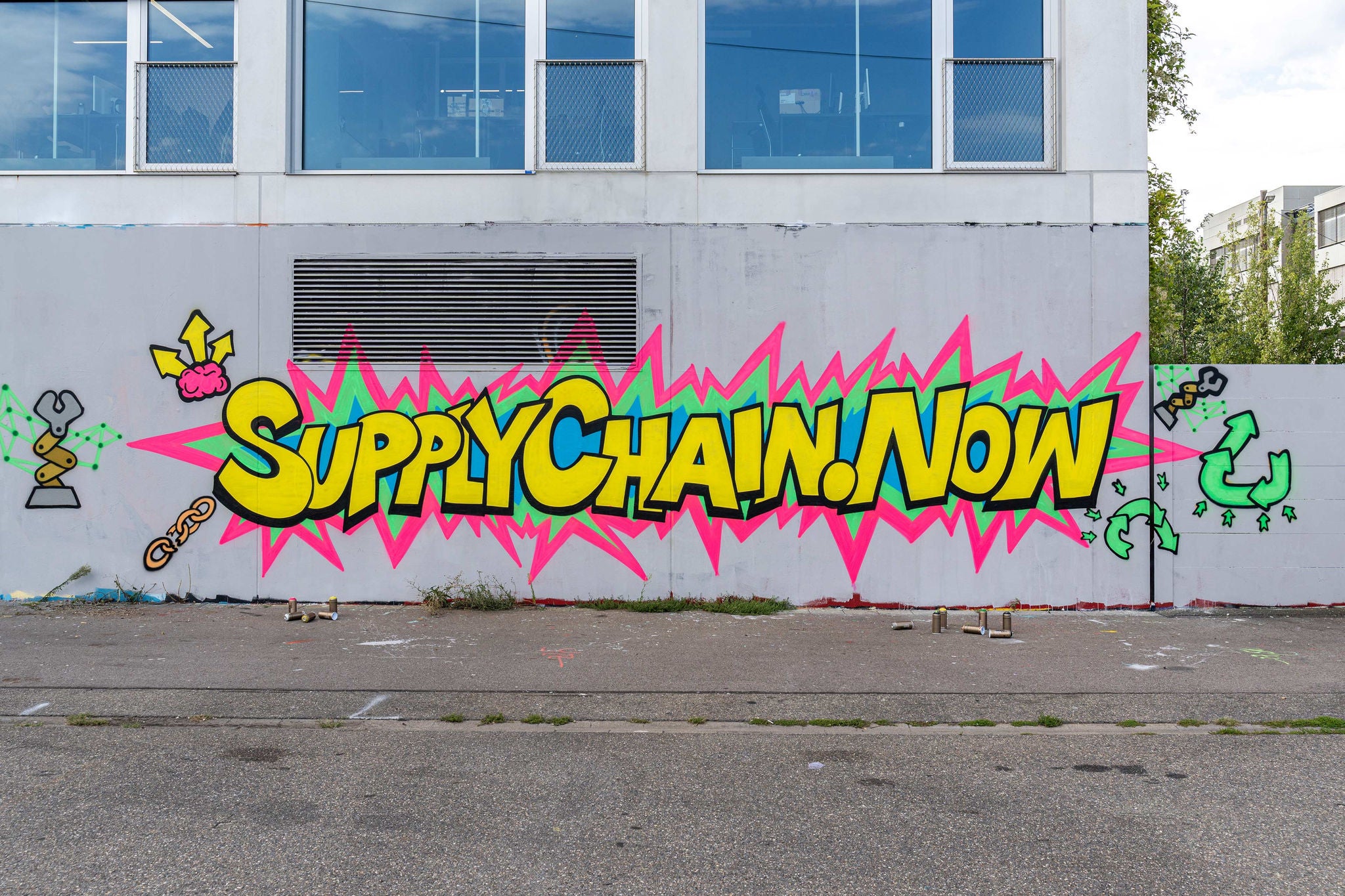 Eine bunte Graffiti-Wand mit dem Schriftzug "Supply Chain Now", der Street Art und zeitgenössische Themen hervorhebt.