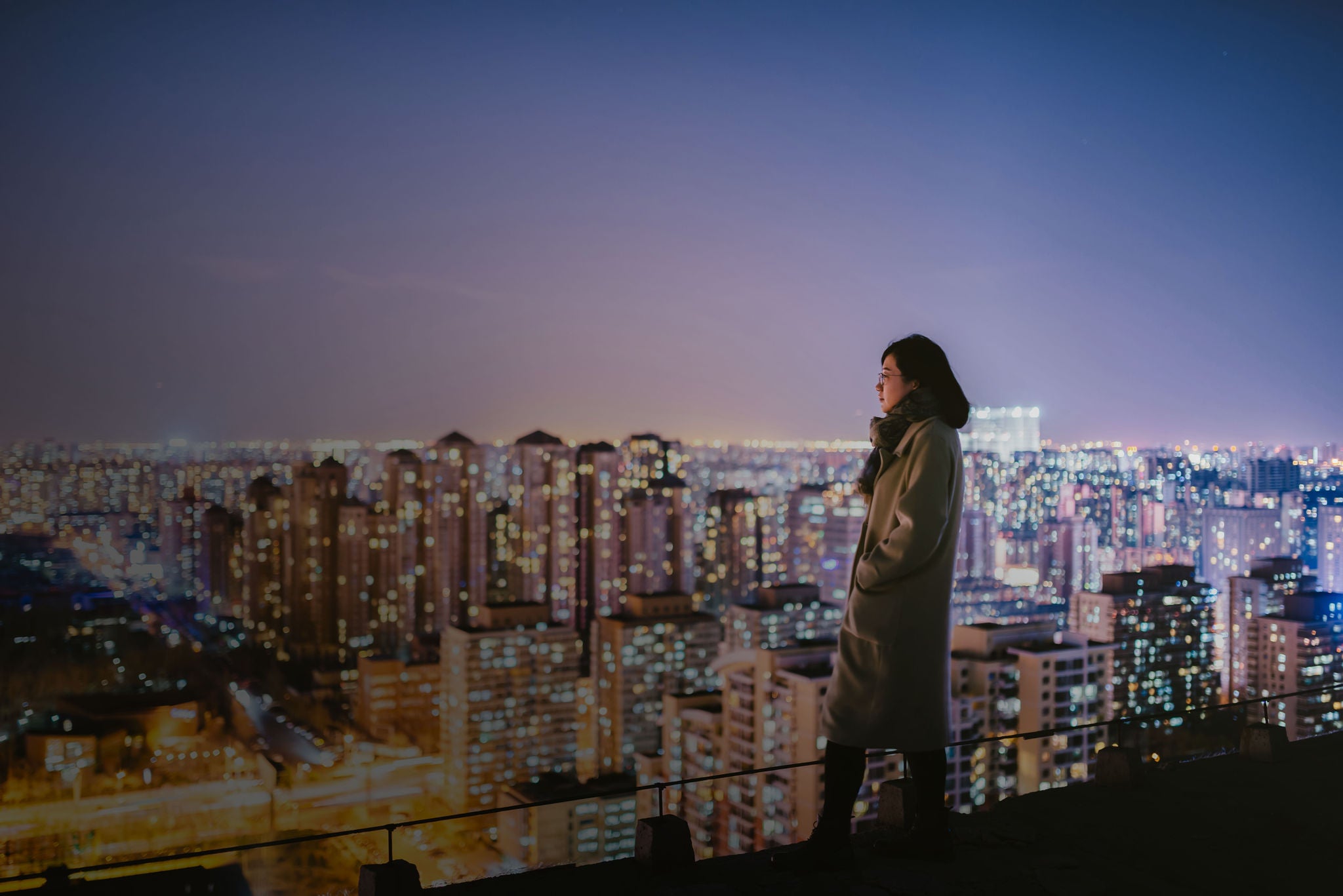 mulher no topo de um prédio olhando uma grande cidade iluminada