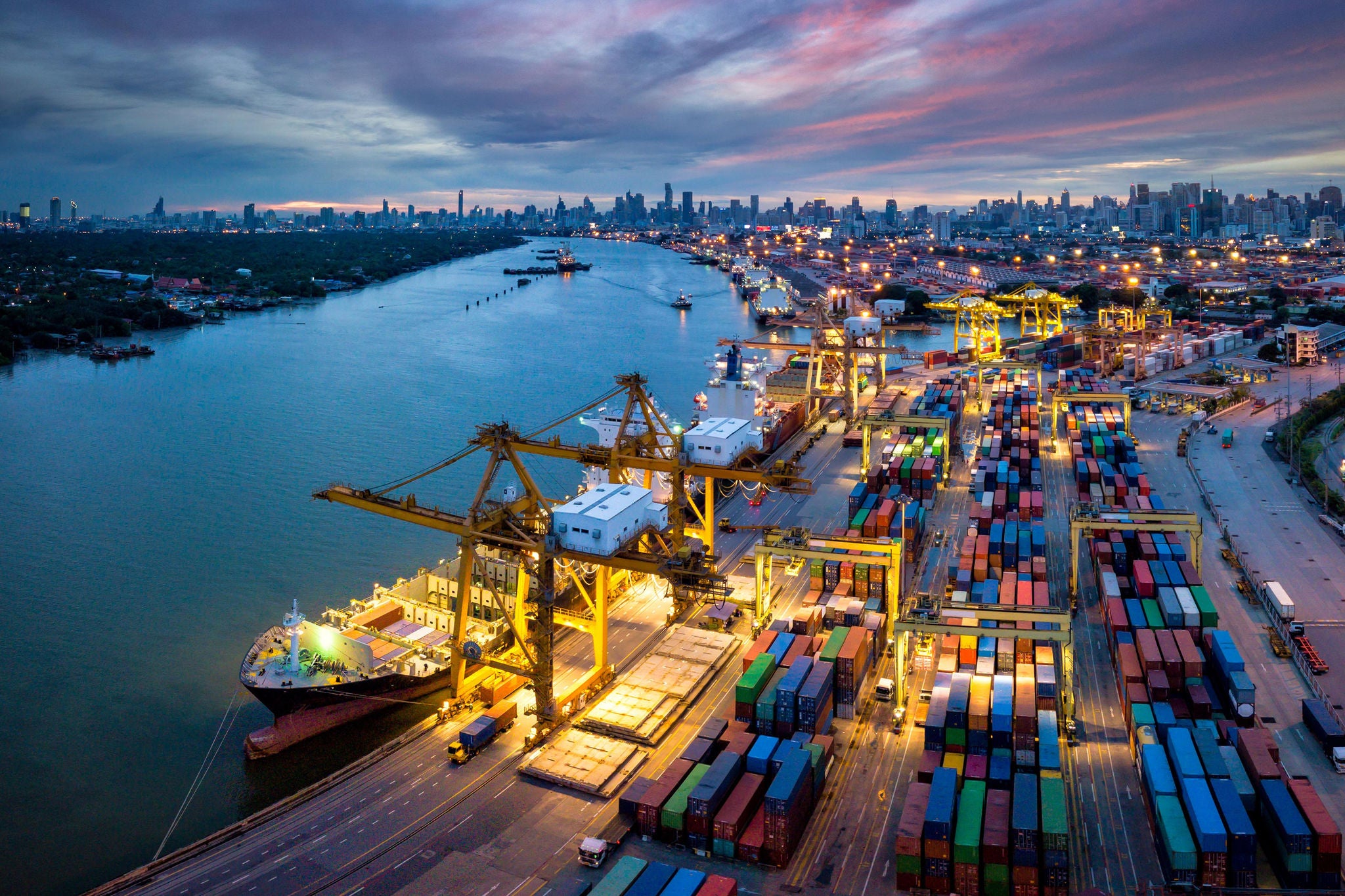 Aerial view of international port with Crane loading containers in import export business logistics with cityscape of Bangkok city Thailand at night