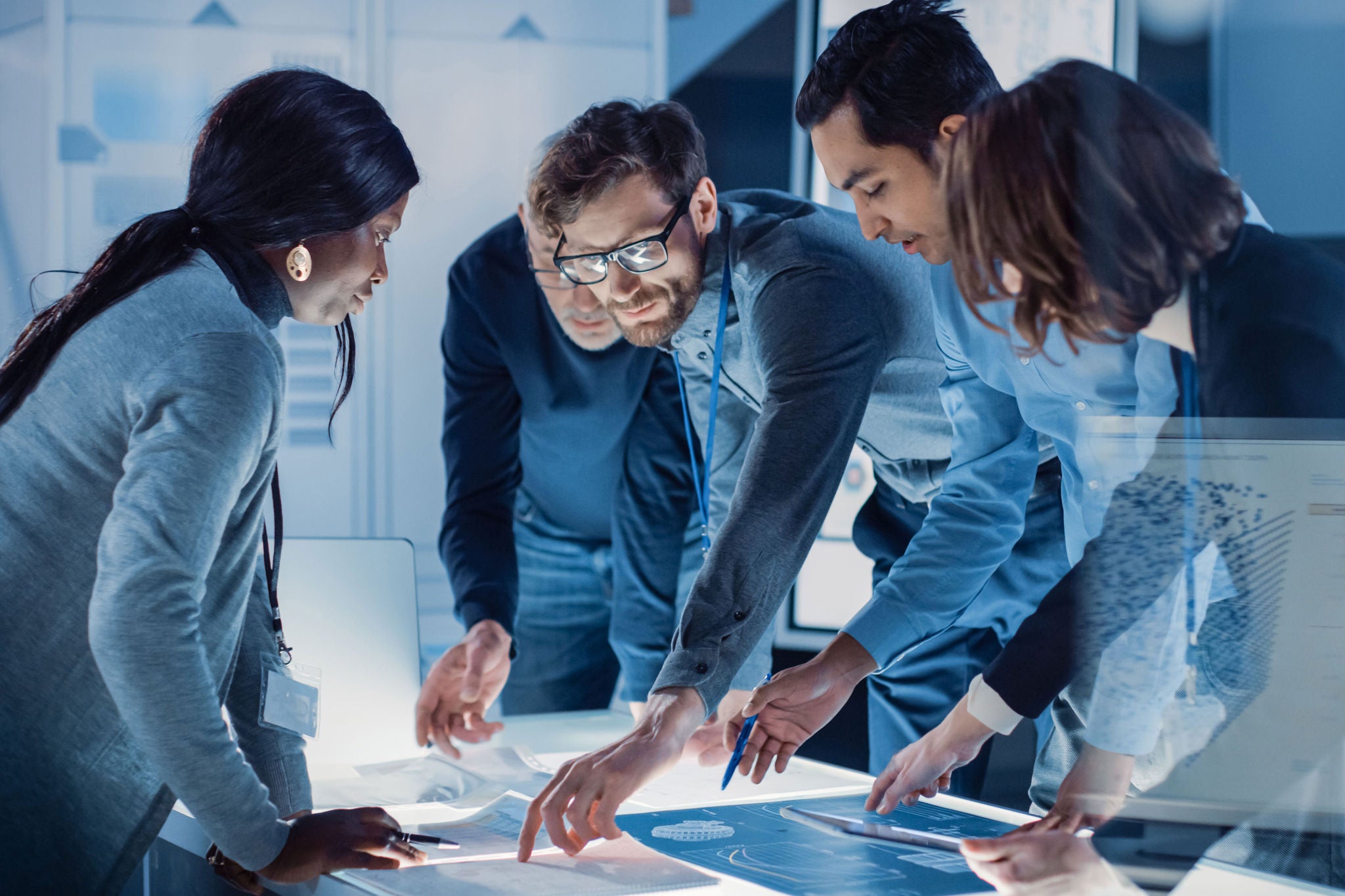 Engineers Meeting in Technology Research Laboratory: Engineers, Scientists and Developers Gathered Around Illuminated Conference Table, Talking and Finding Solution, Inspecting and Analysing Industrial Engine Design.