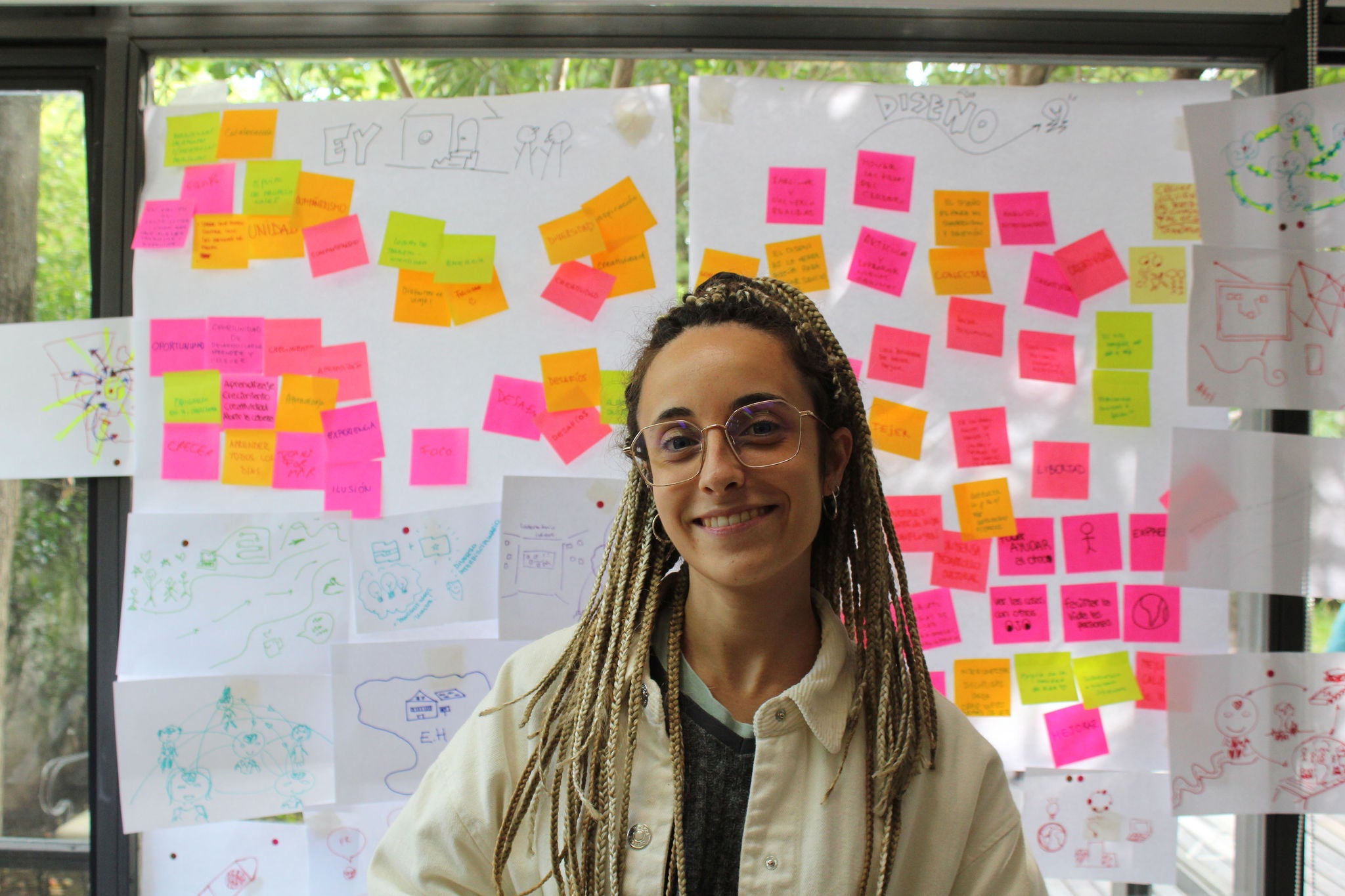 Mujer mirando sonriente a la cámara con una pared con post its de fondo