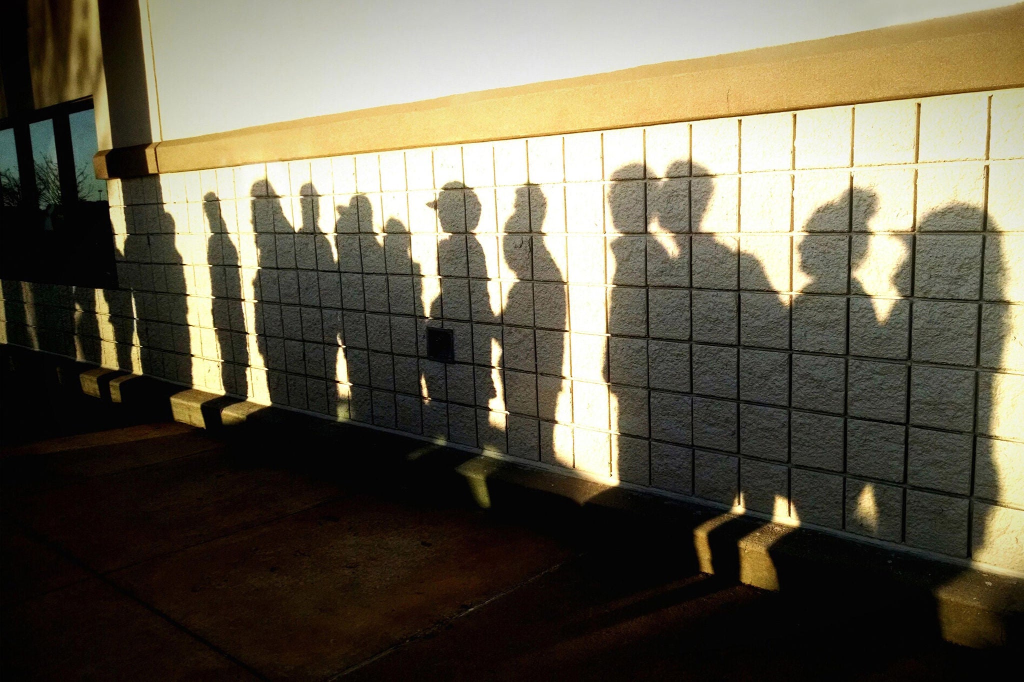 Shadow of men and women standing in queue on wall.