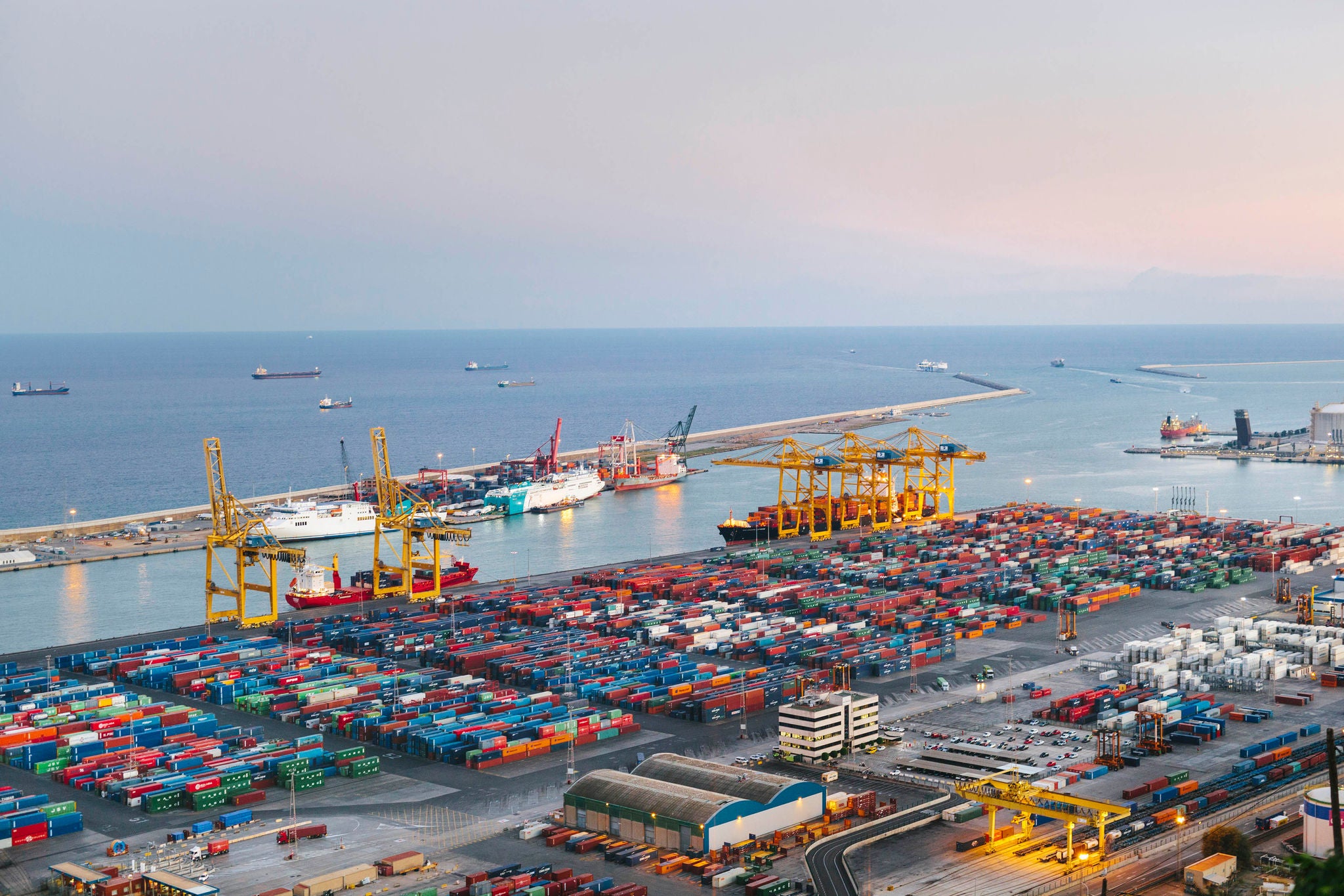 Barcelona commercial dock at dusk with containers and cranes.