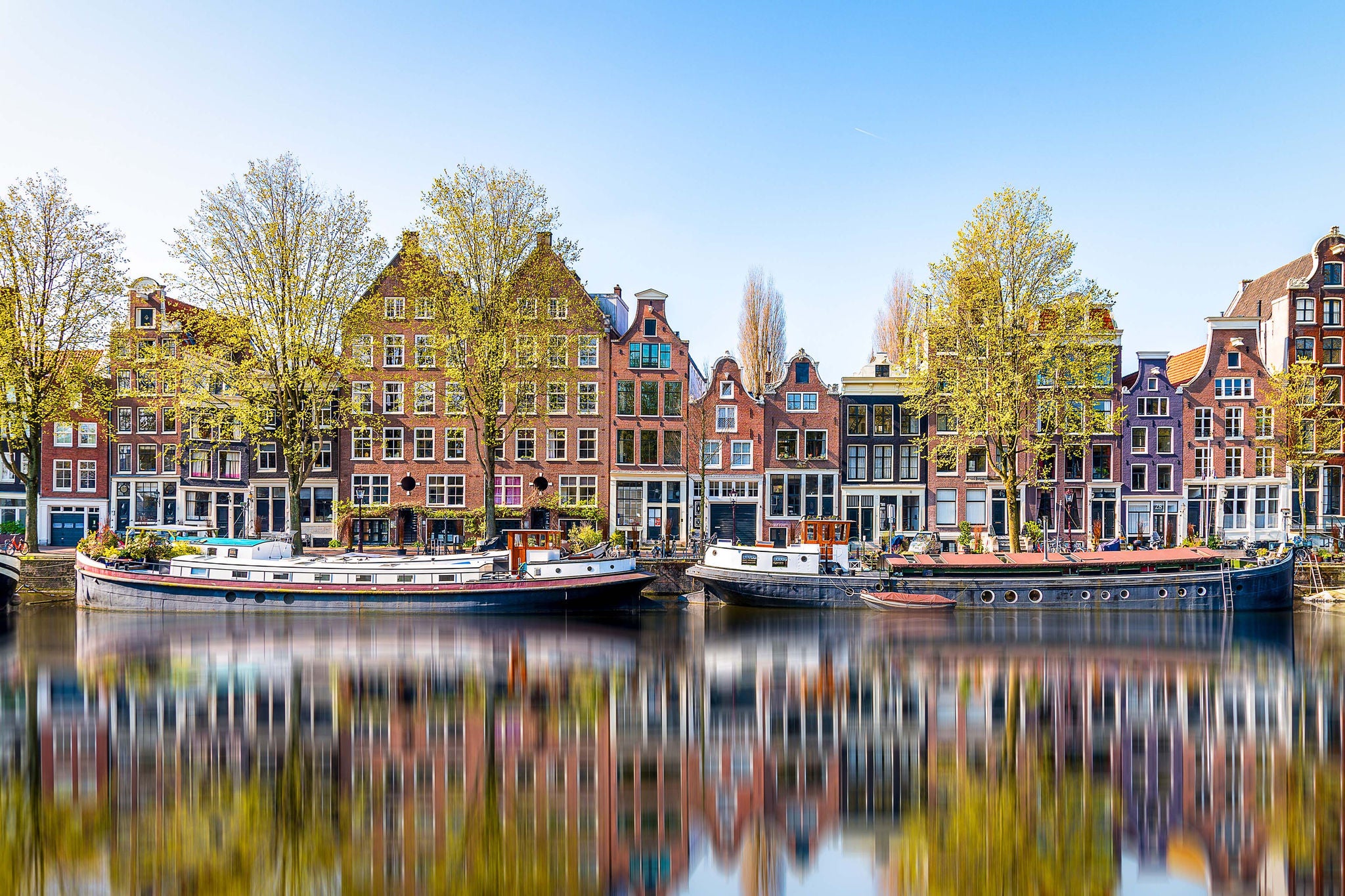 In einer Gracht in Amsterdam reflektieren sich die historischen Haeuser und der blaue Himmel am Morgen