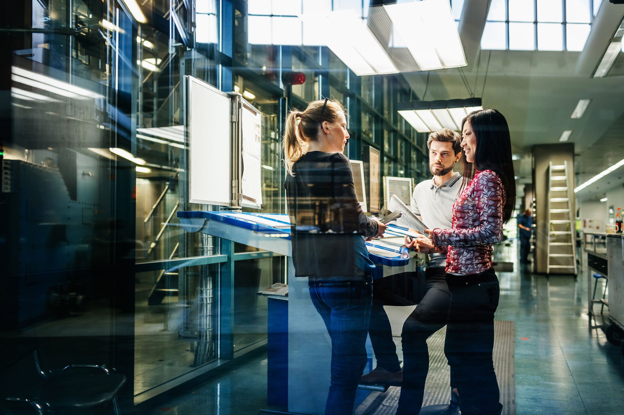 A team of engineers having a discussion at a desk in a large printing factory.