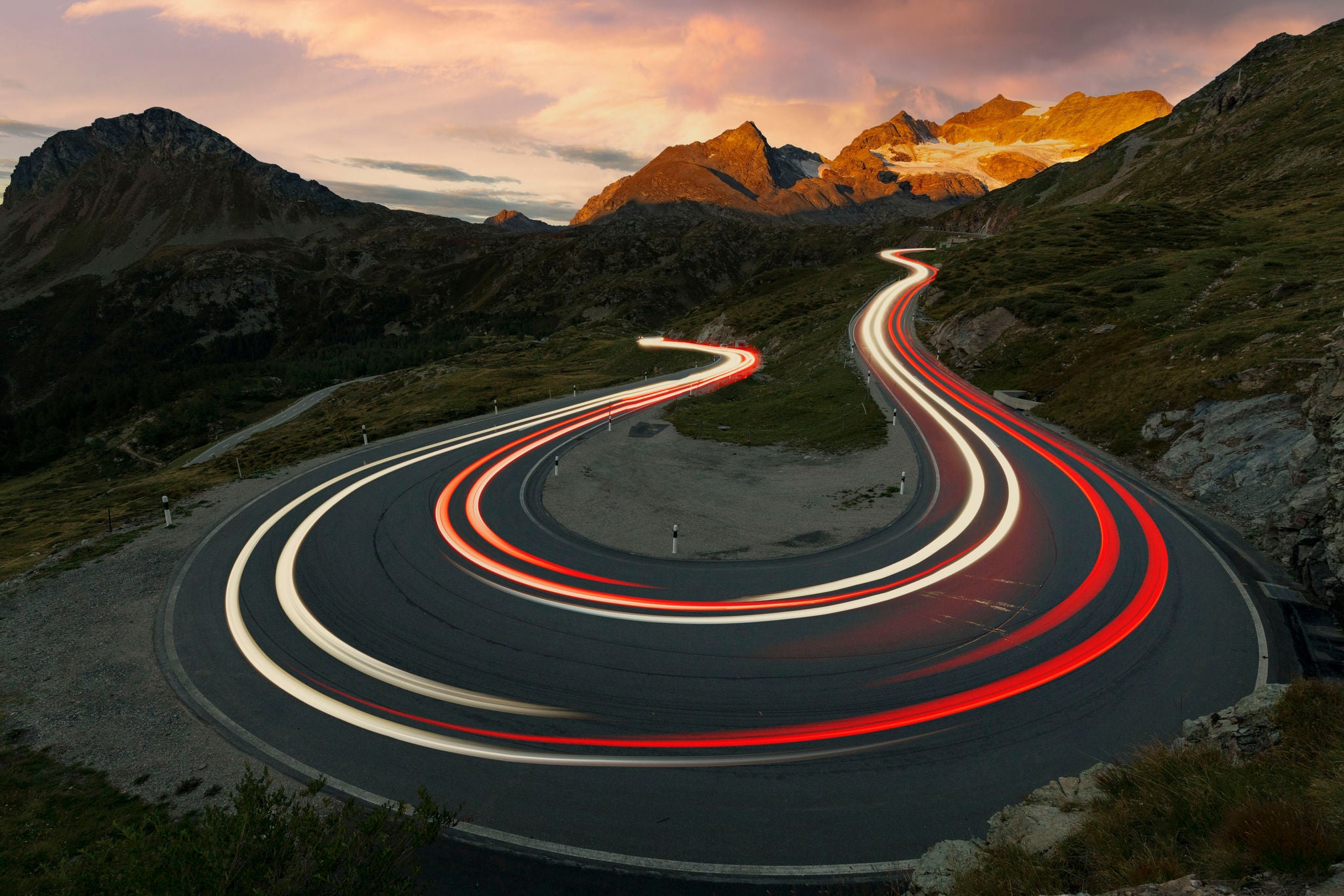 Lights of car trails on Bernina Pass mountain road at sunrise, Val Poschiavo, canton of Graubunden, Switzerland