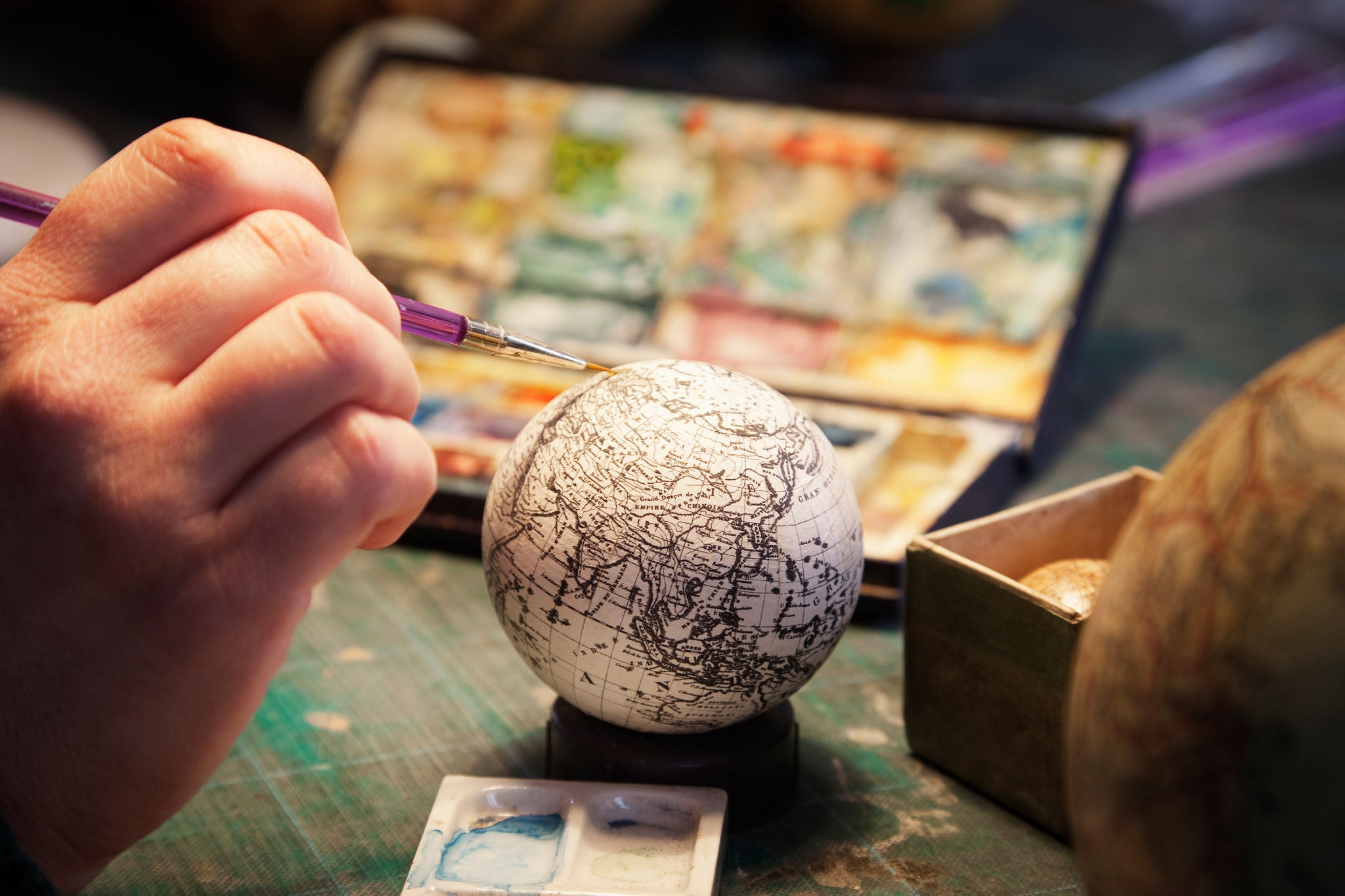 Cartographer using colour paint to add detail to small globe