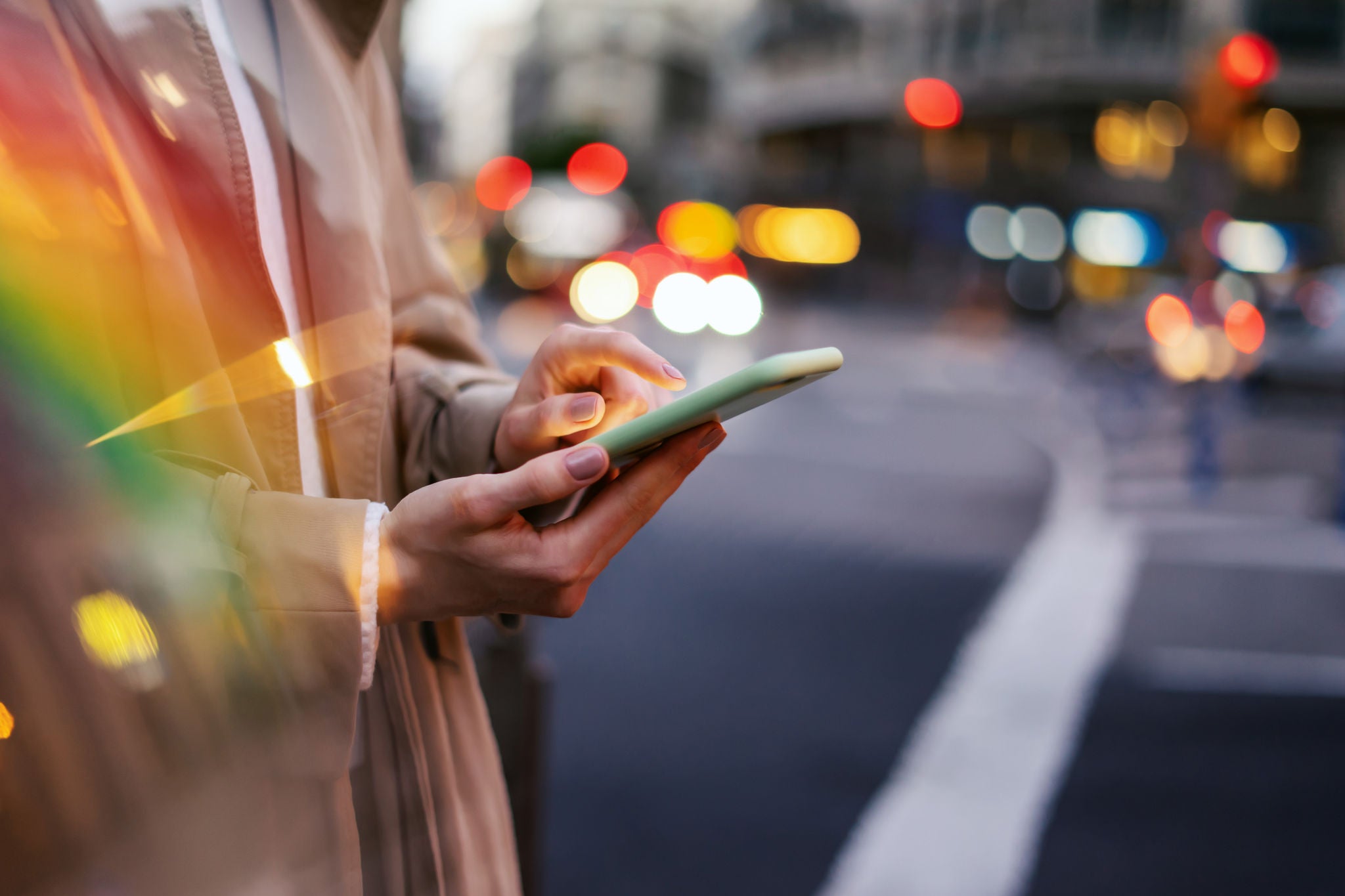 Closeup photo of female hands holding smartphone. Night street with lights on background