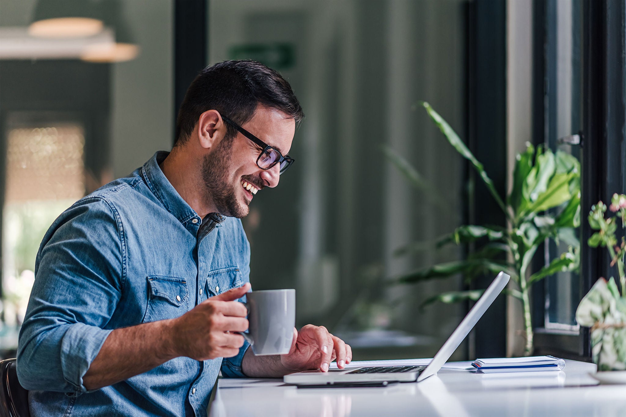 Mann drikker kaffe mens han smiler og jobber på pc