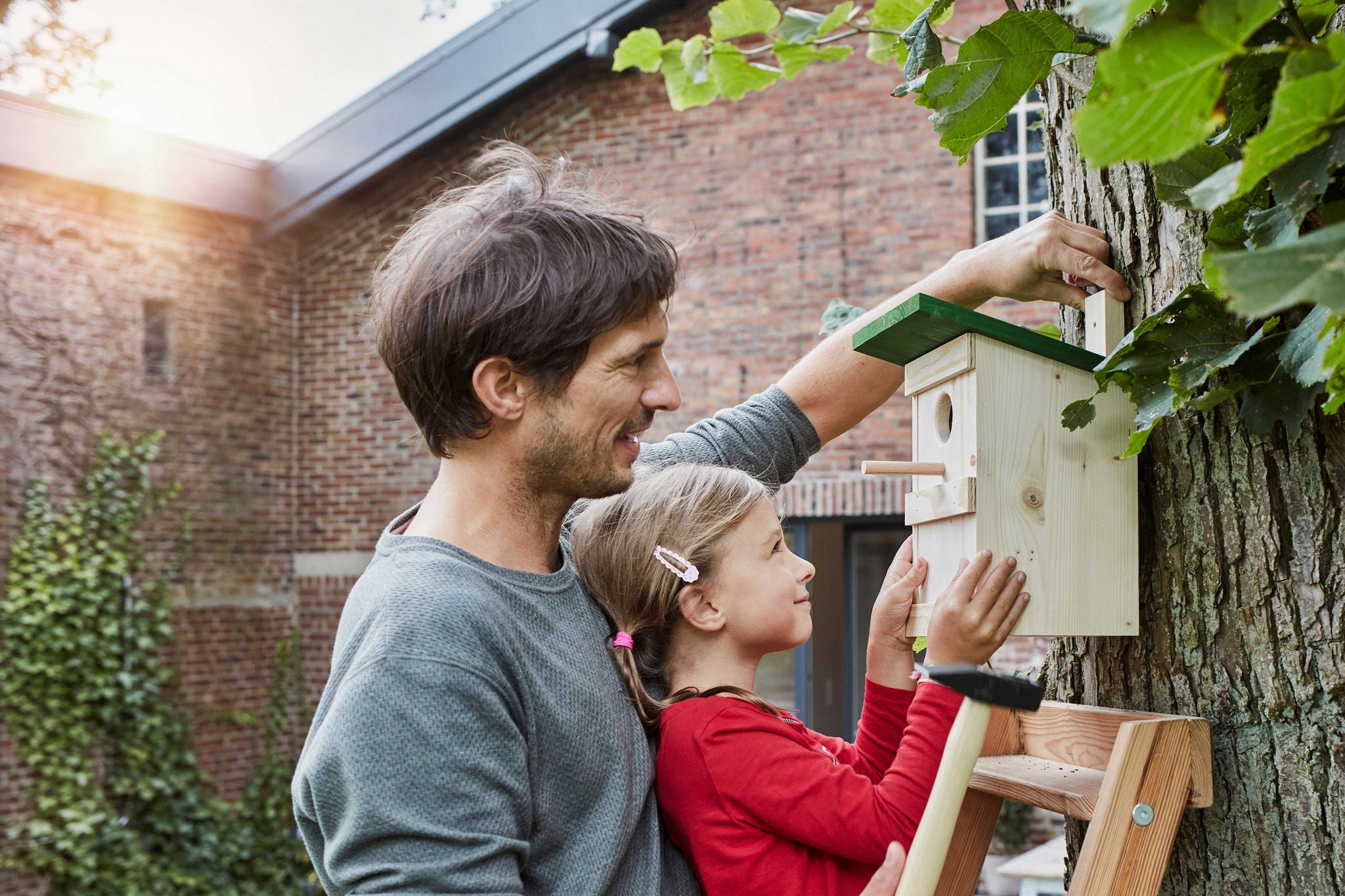 Vater und Tochter haengen Nistkasten im Garten auf