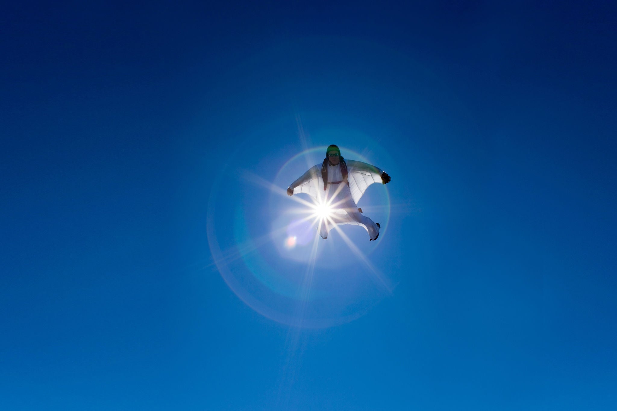 aerial view of flying white wingsuit with sunflare