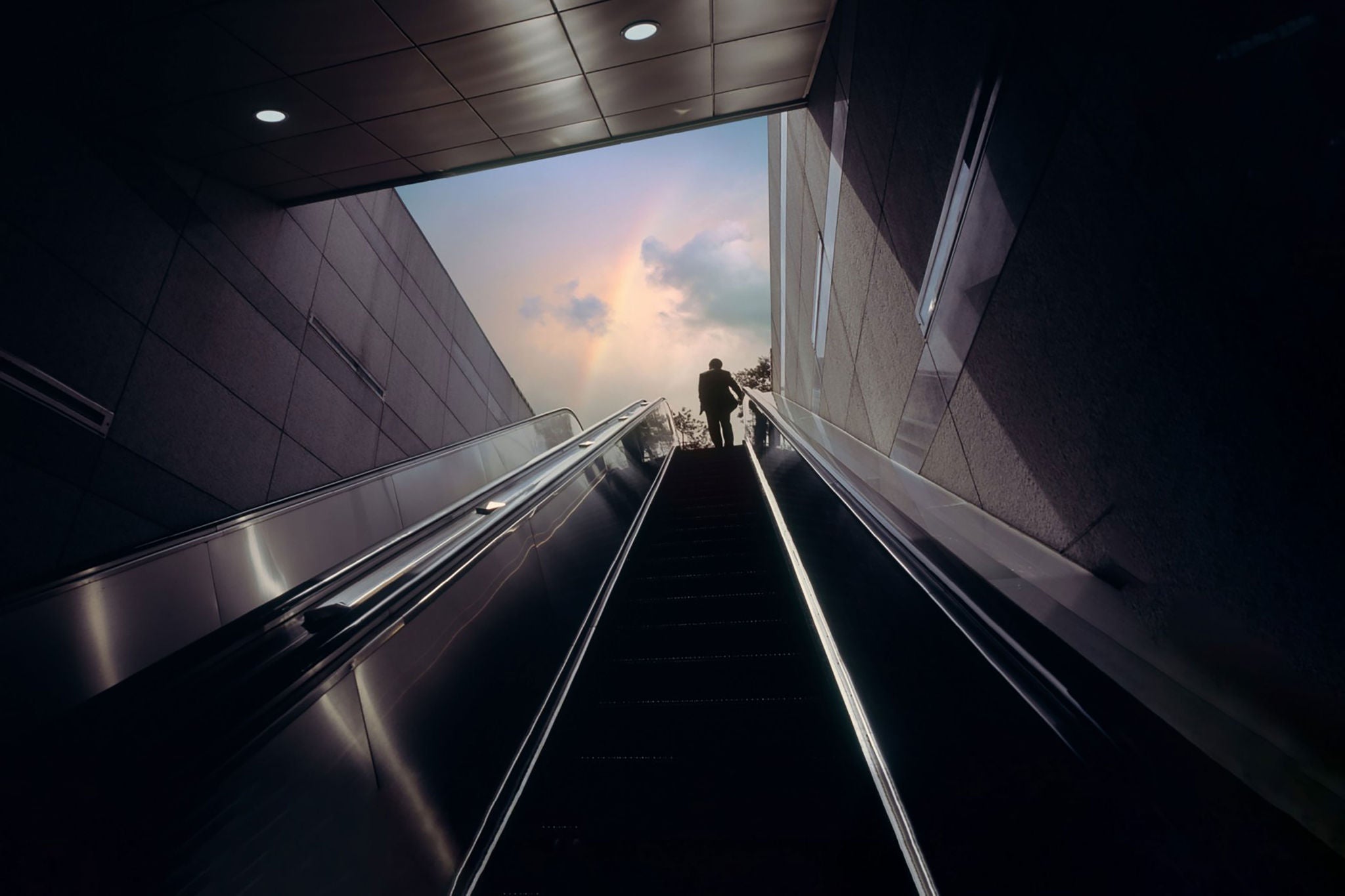 Businessman on escalator moving towards sky with rainbow