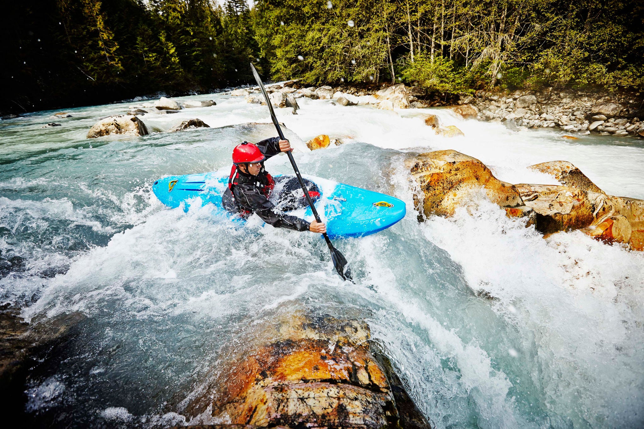 Kayaker entering white water rapids between narrow gap in rocks