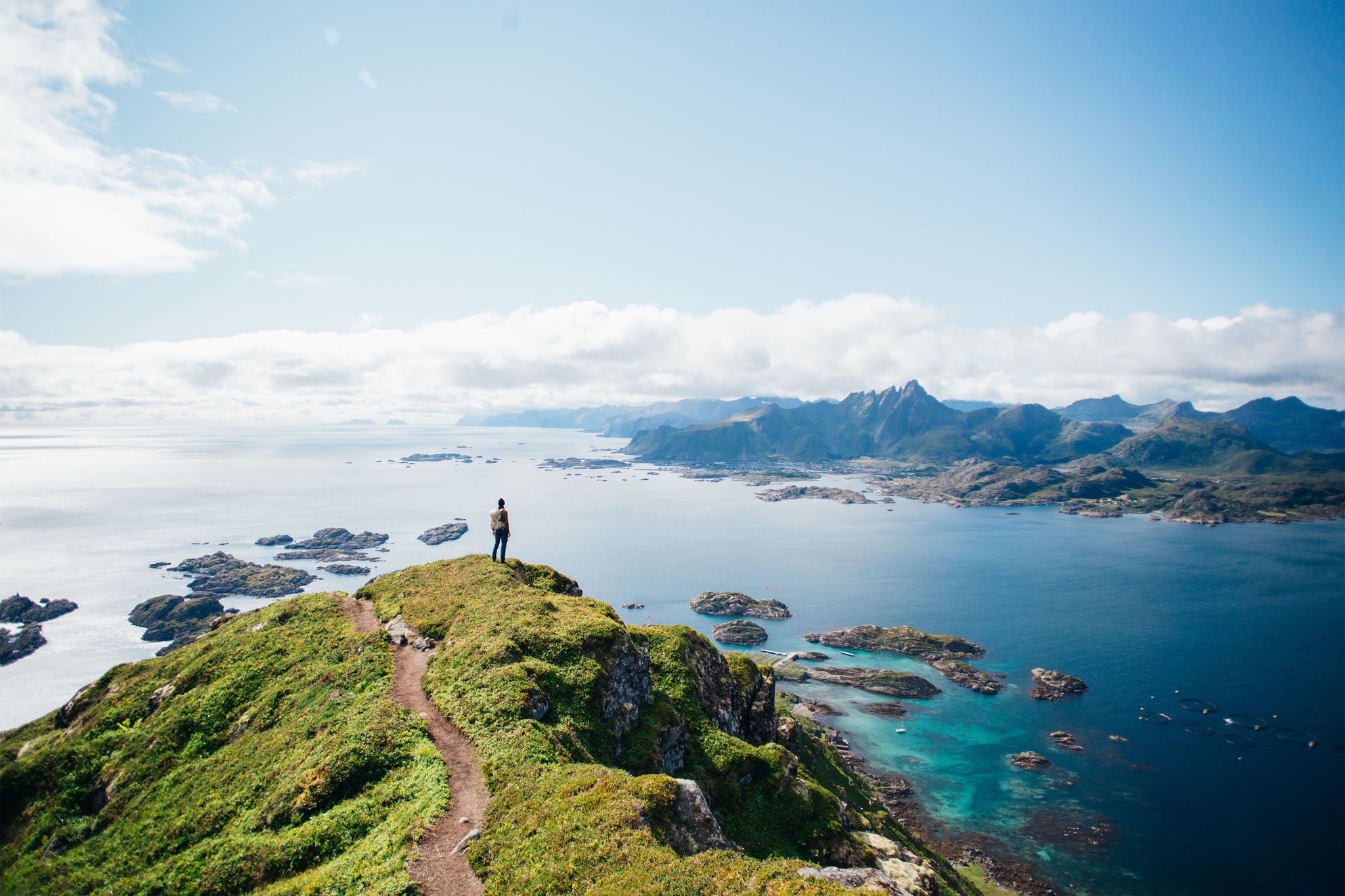 Amazing epic shot of young man hiker stand on top of mountain after long difficult hike in Lofoten Islands in Norway. Incredible summer views of scandinavian travel lifestyle. Epic landscape in north