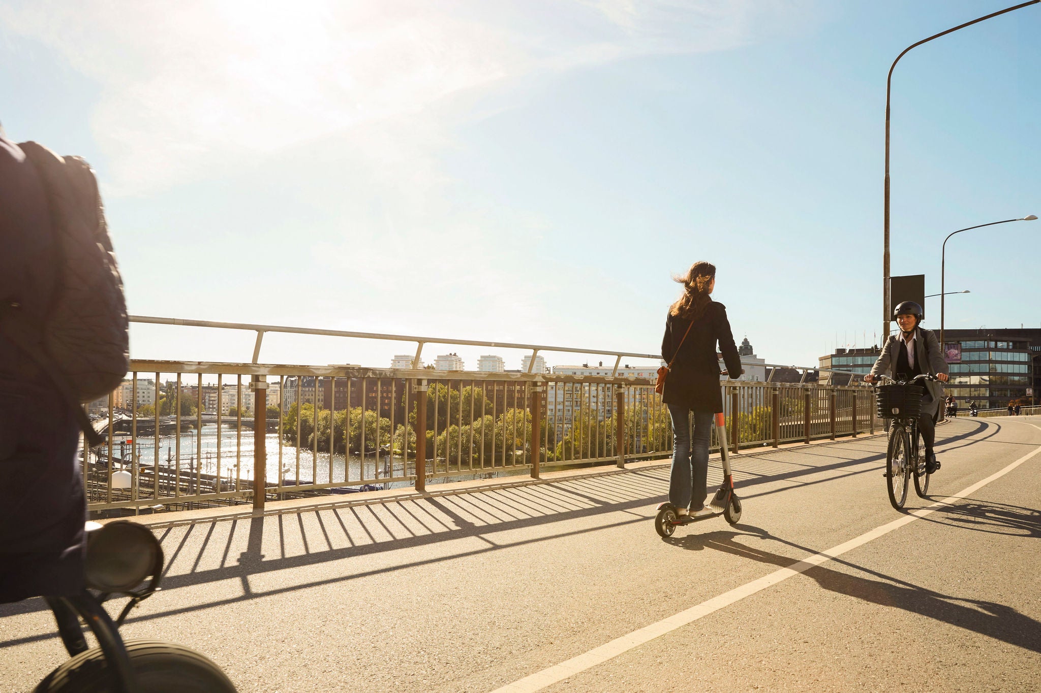 Commuters riding electric vehicles on bridge against blue sky